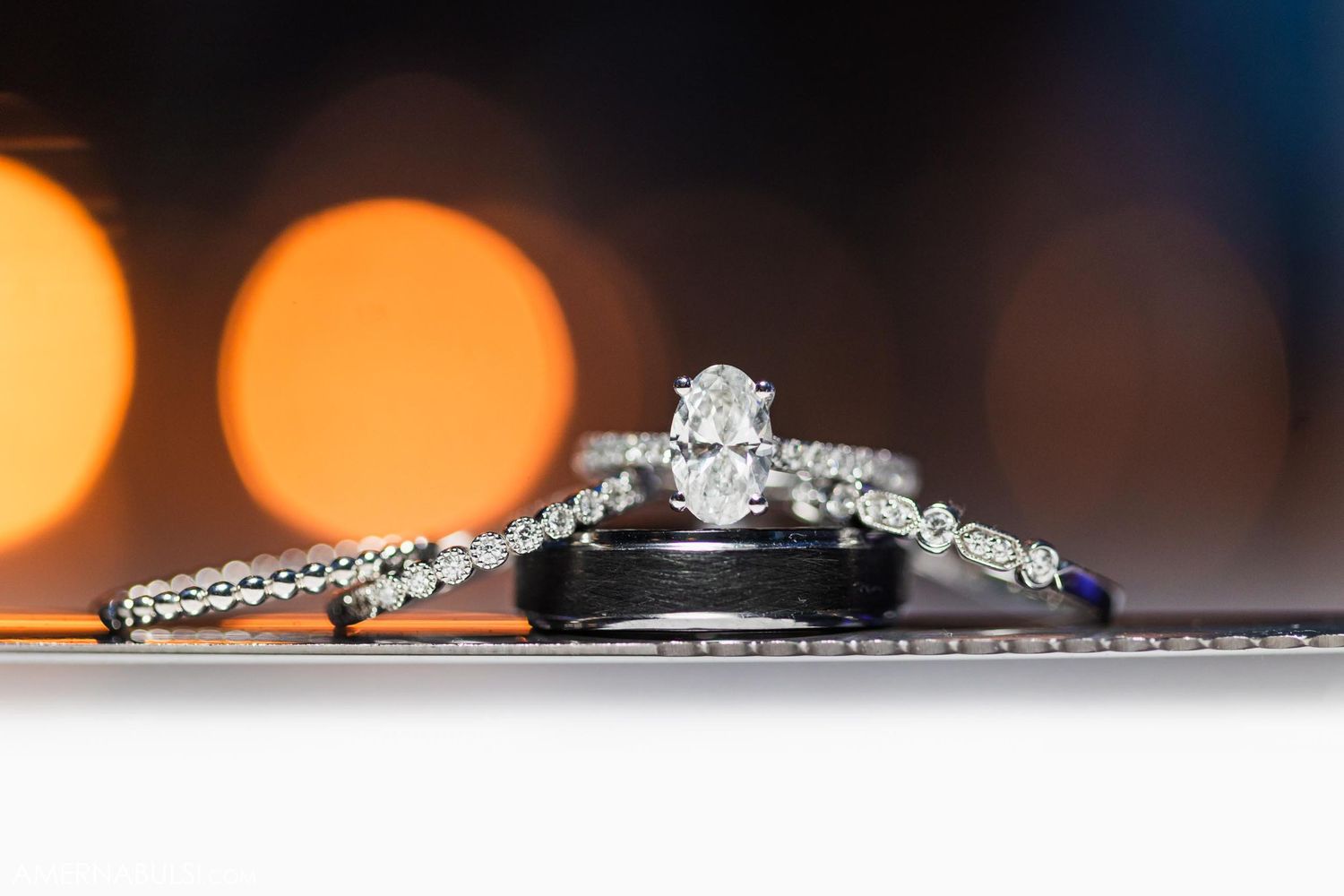 Diamond engagement ring and wedding bands arranged artistically with bokeh background lighting.