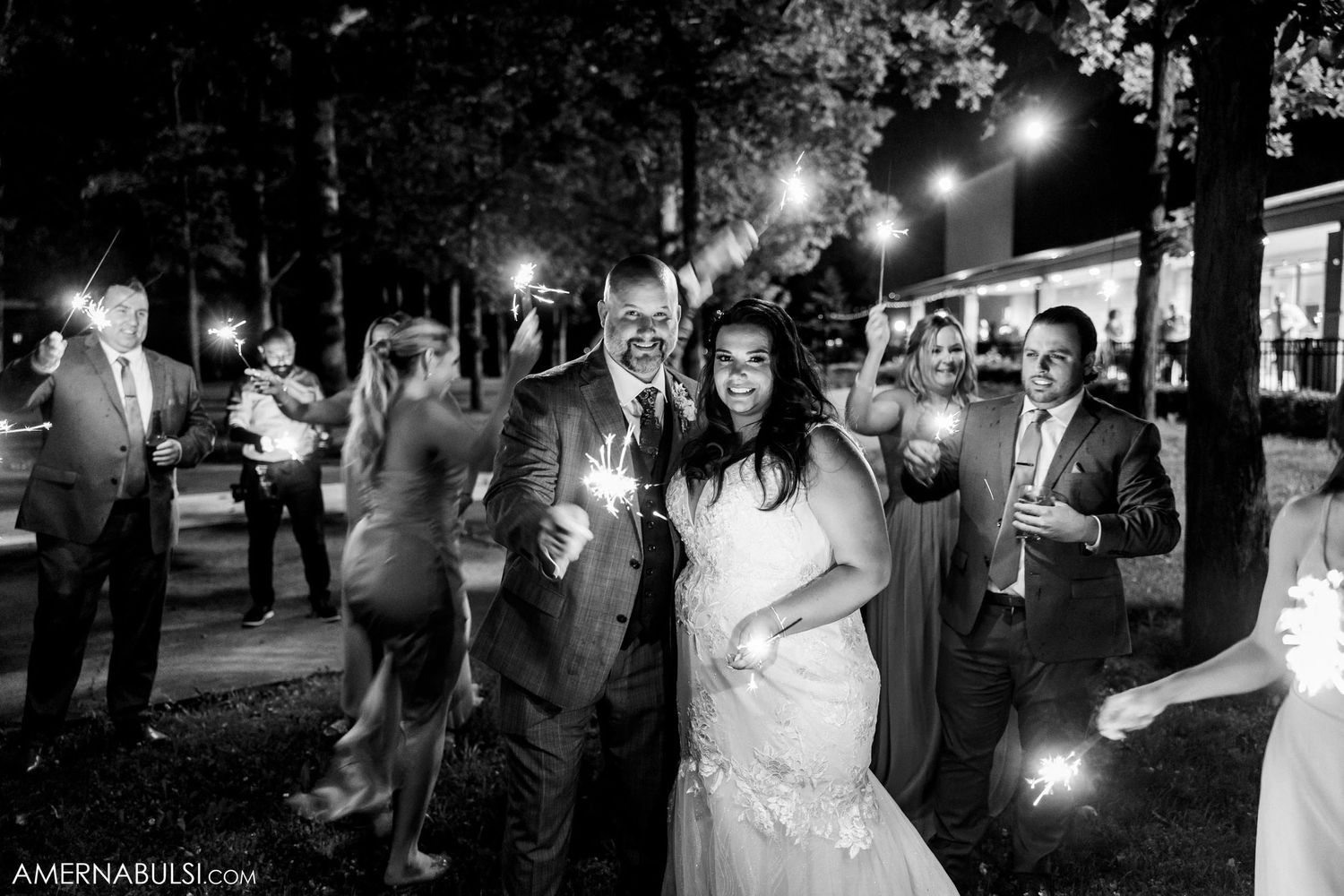 Wedding party celebrates with sparklers during an evening outdoor reception.