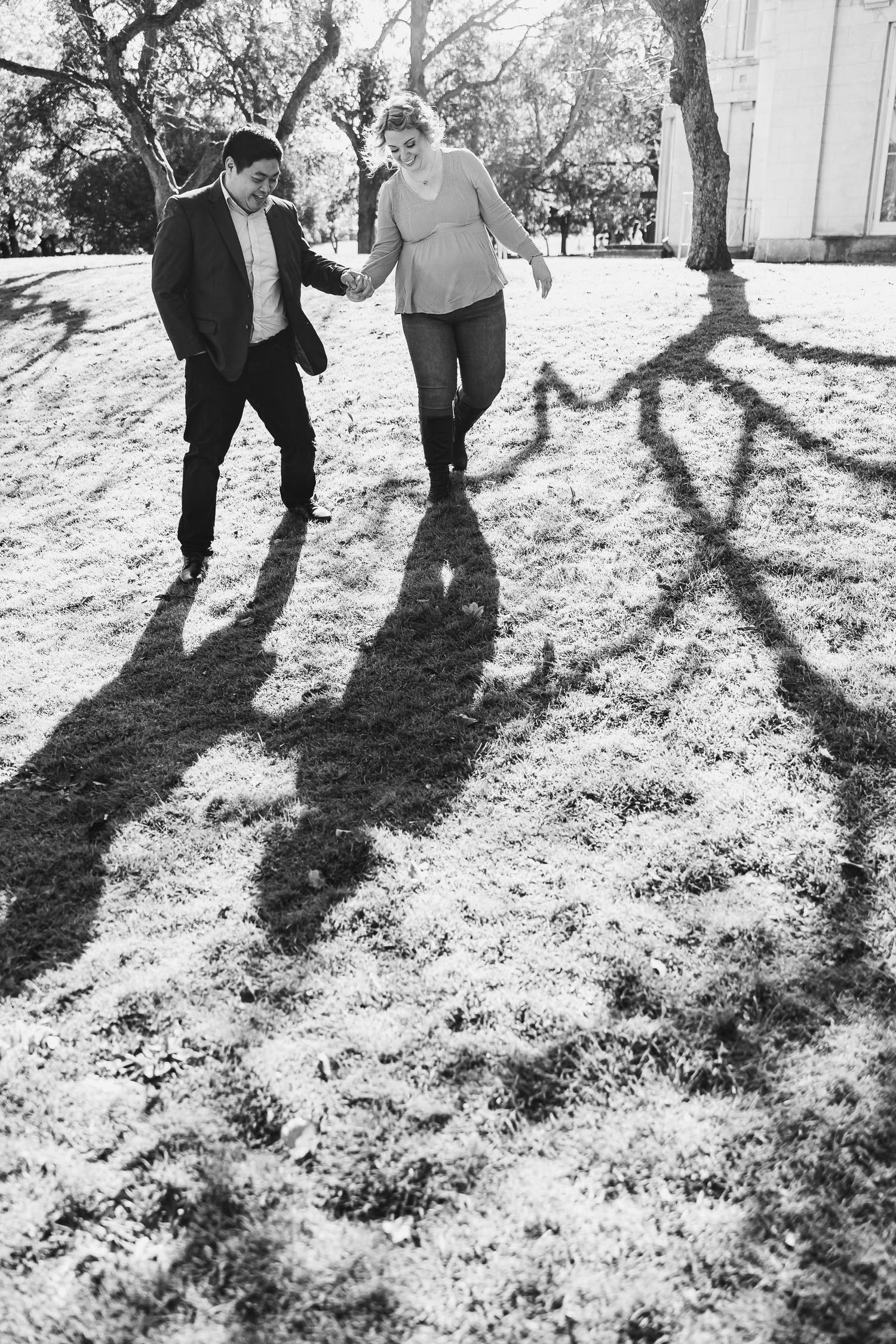 Two people dance and laugh together casting long shadows on sunny grass.