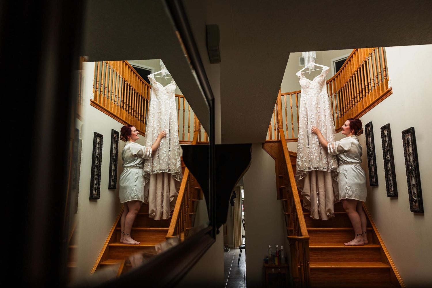 Wedding dress hanging on staircase with mirror reflection creating symmetrical composition.