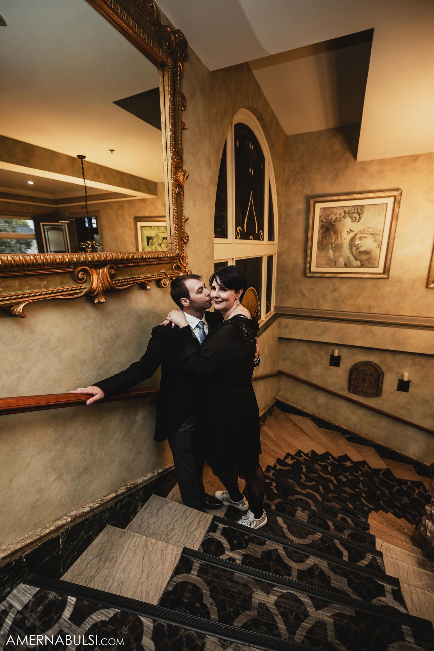 Elegant staircase with ornate gold-framed mirrors and patterned carpet in a historic venue.