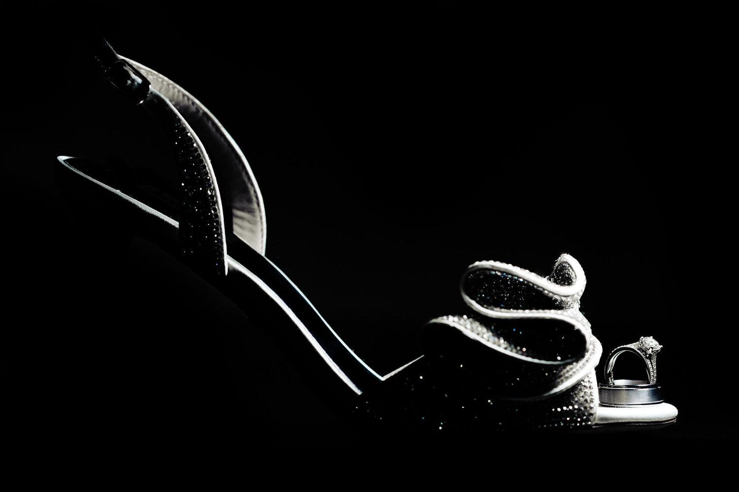 Artistic black and white photo of elegant bridal heels against dark background.