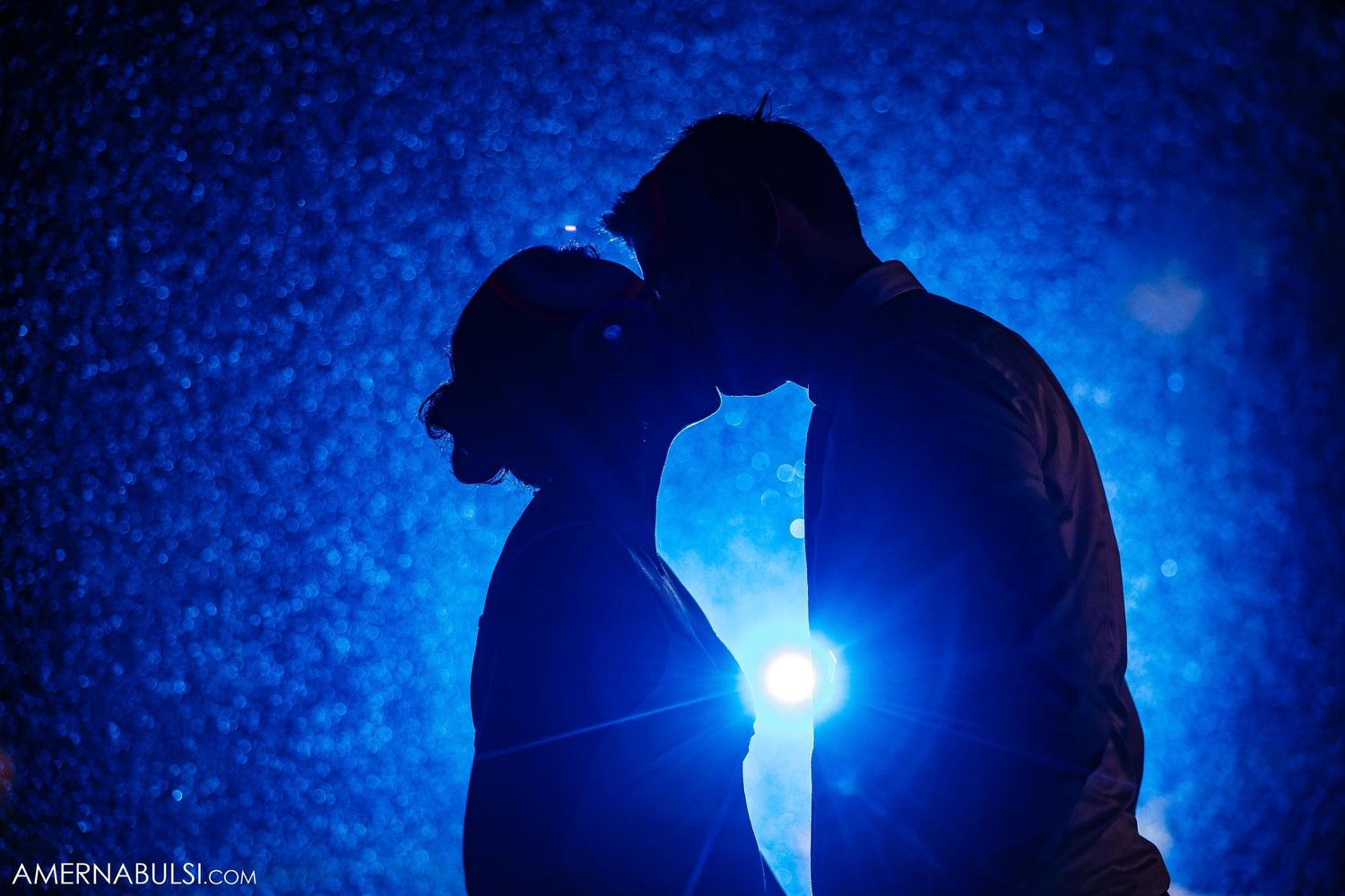 Silhouetted couple against dramatic blue backlight creating intimate atmosphere.