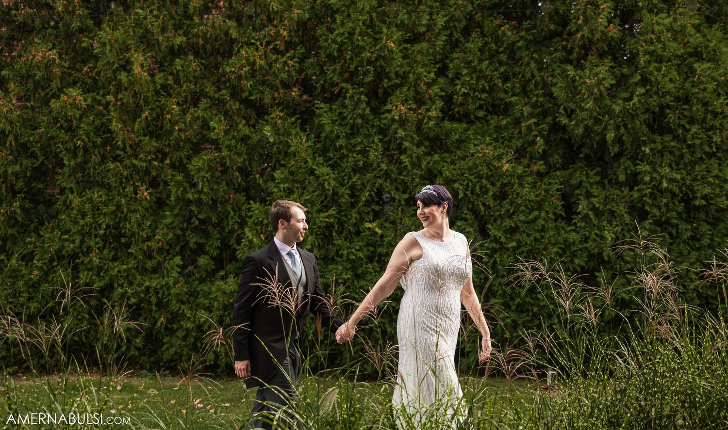 Candid wedding moment captured against lush green garden backdrop.