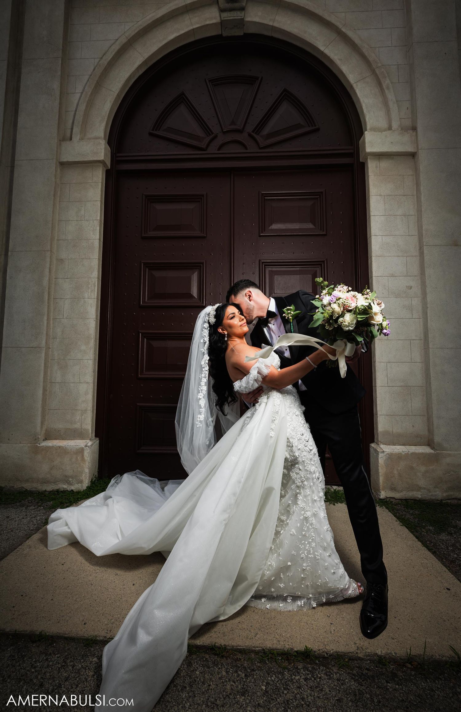 Romantic wedding portrait in front of a grand wooden arched doorway.