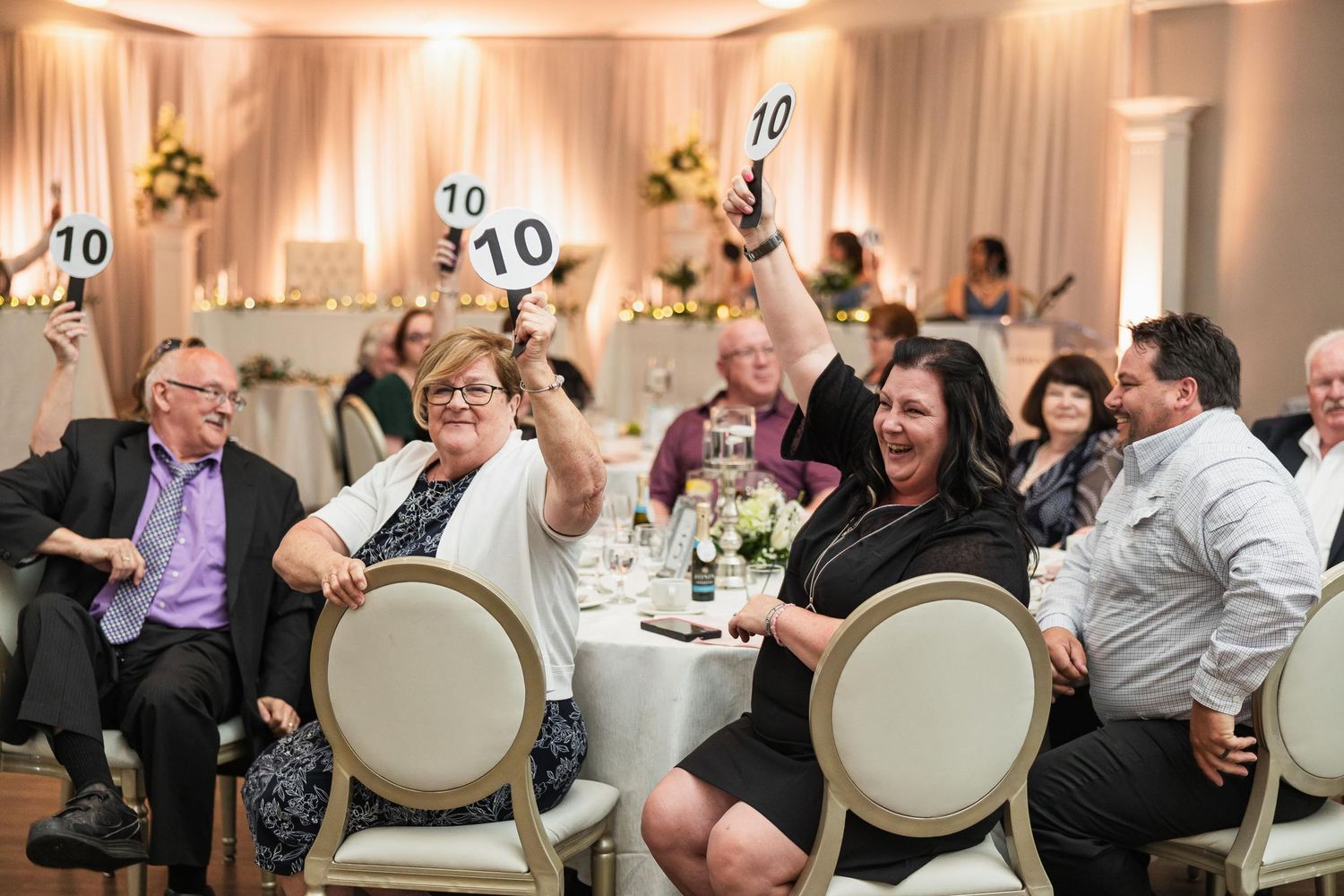 Wedding guests holding up score cards and cheering during a reception event in an elegant ballroom.