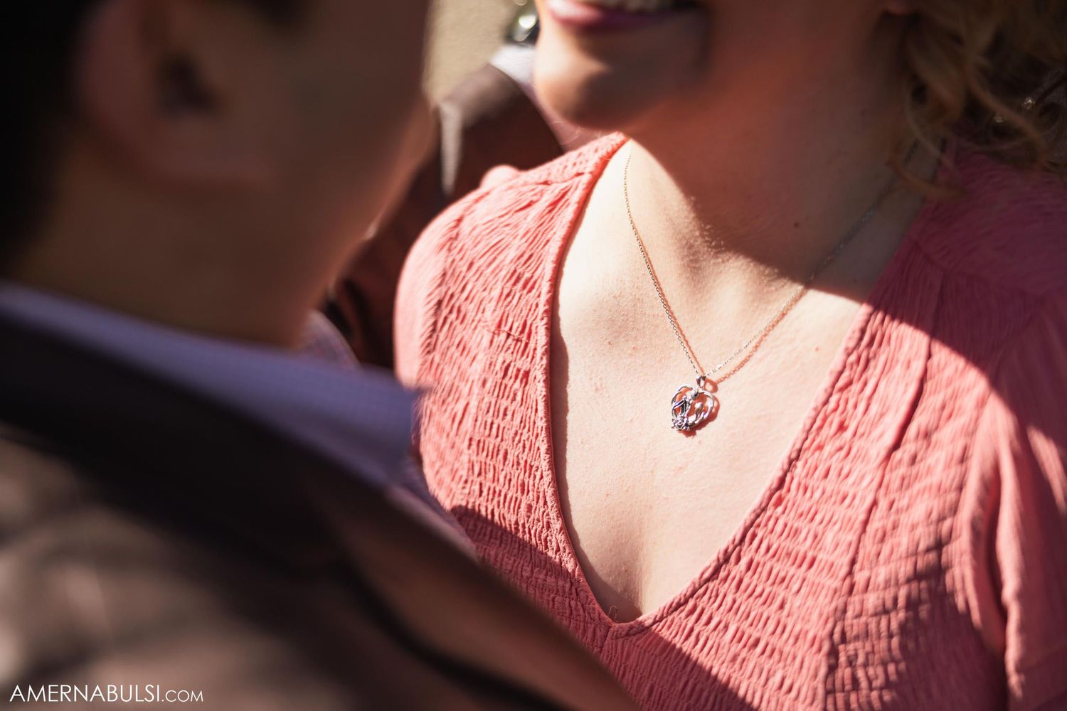 Close up detail of pink blouse and delicate necklace in sunlight.