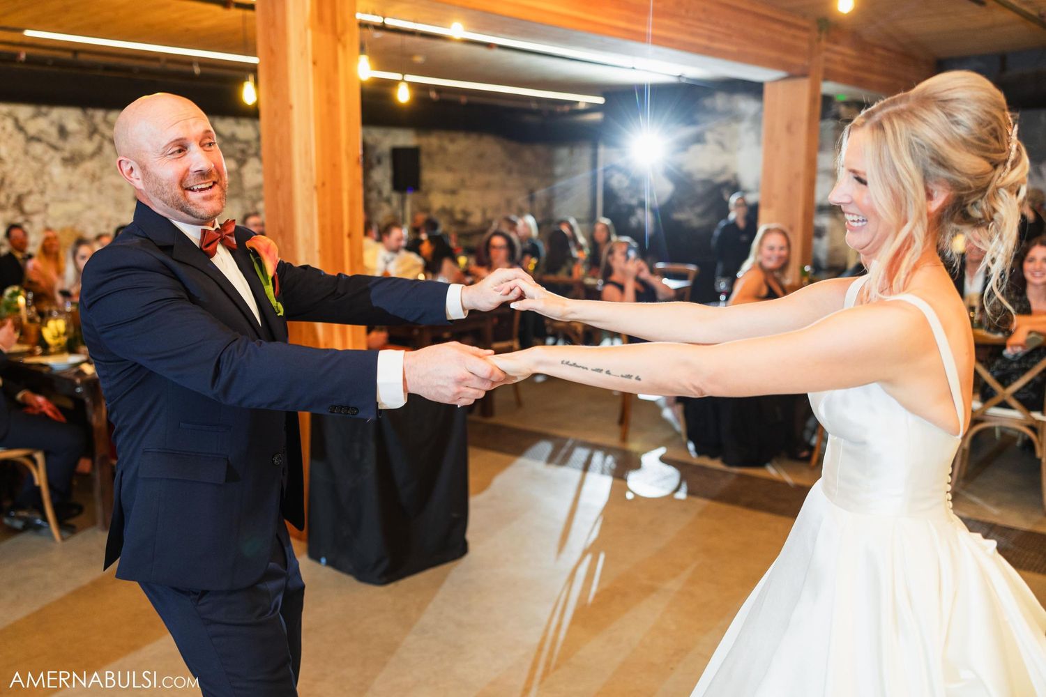 A couple shares a playful dance moment at their wedding reception in a rustic wooden venue.
