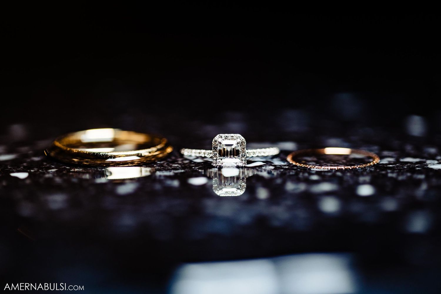 Close-up of wedding rings and jewelry with dramatic lighting on reflective surface.