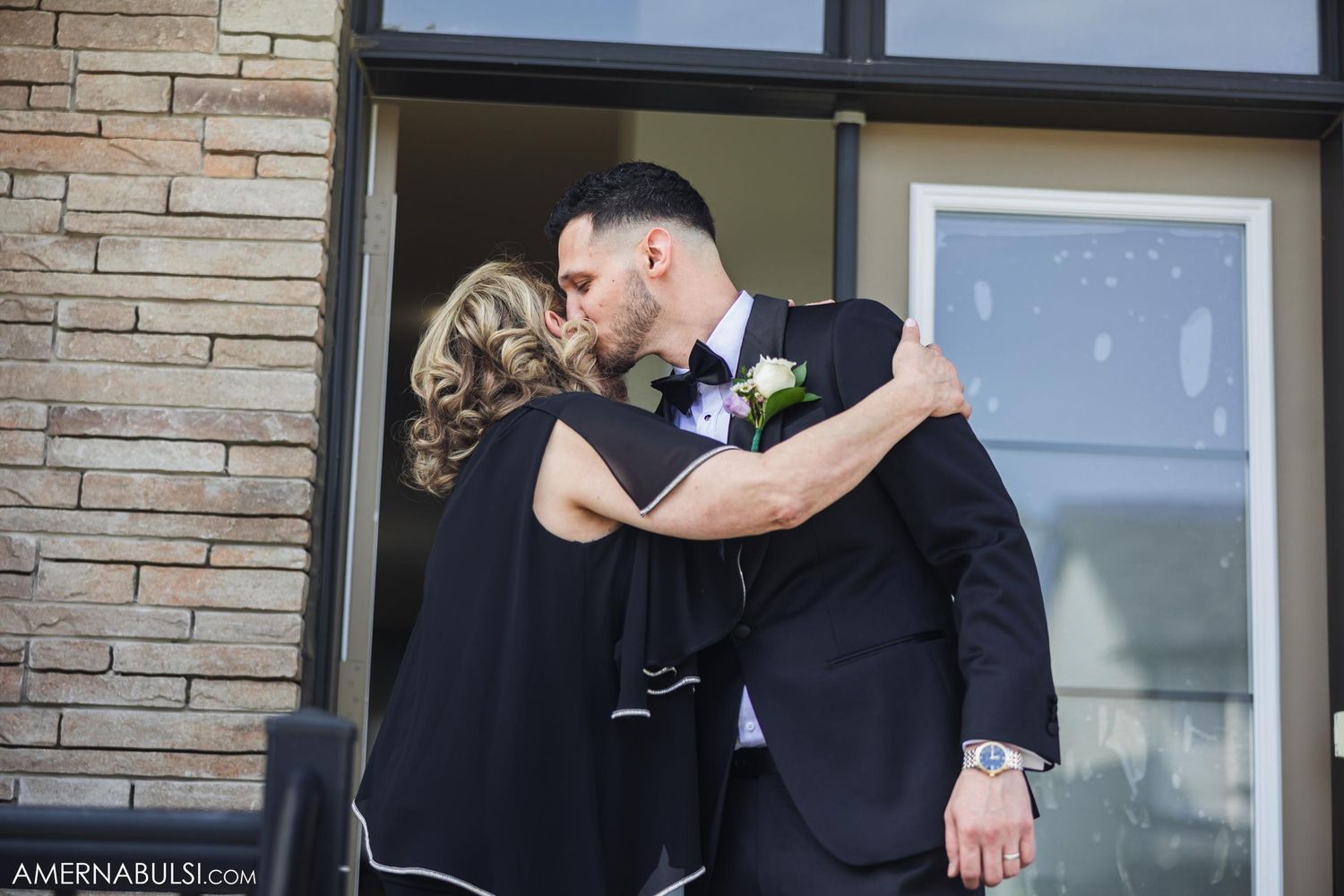 A couple sharing an affectionate moment outside a modern stone building entrance.