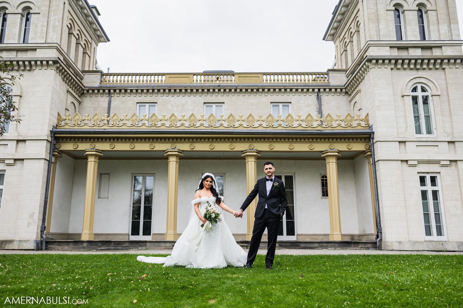 Wedding couple standing in front of grand historic mansion with classical architecture.