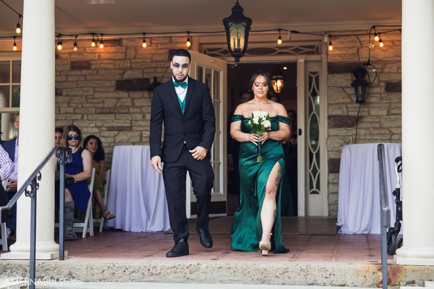 A formal couple descending stone steps at an elegant venue with string lights.