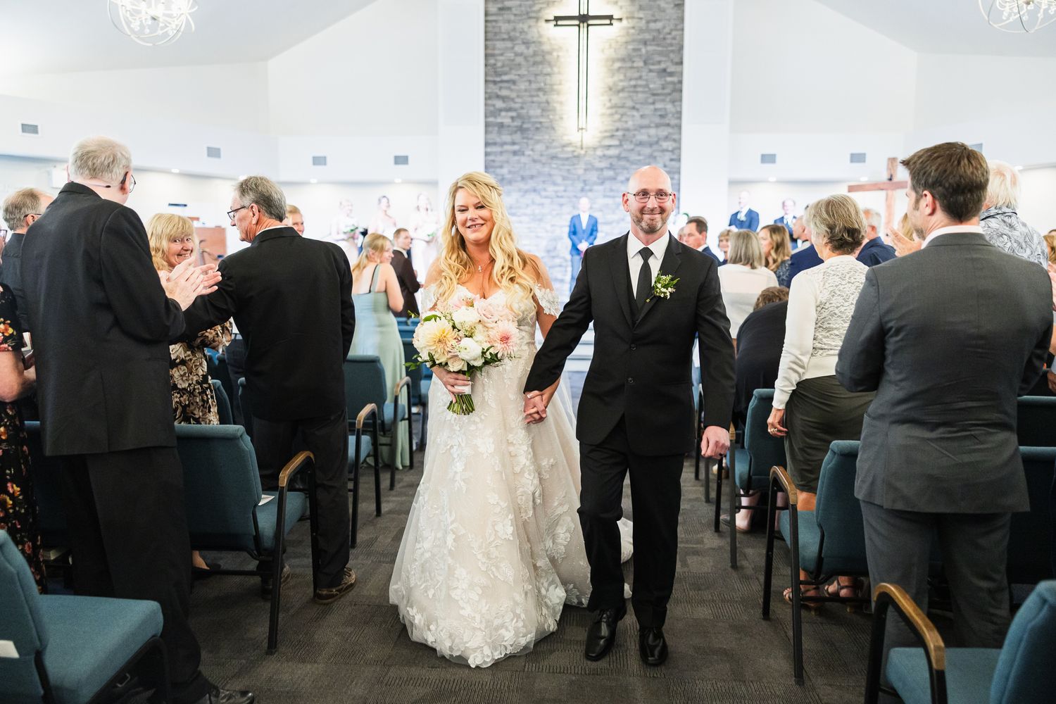 Wedding ceremony venue with modern stone wall and chandelier lighting as guests look on.
