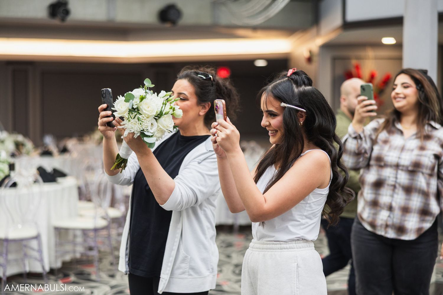 Wedding celebration with guests taking photos and enjoying festivities in a decorated indoor venue.