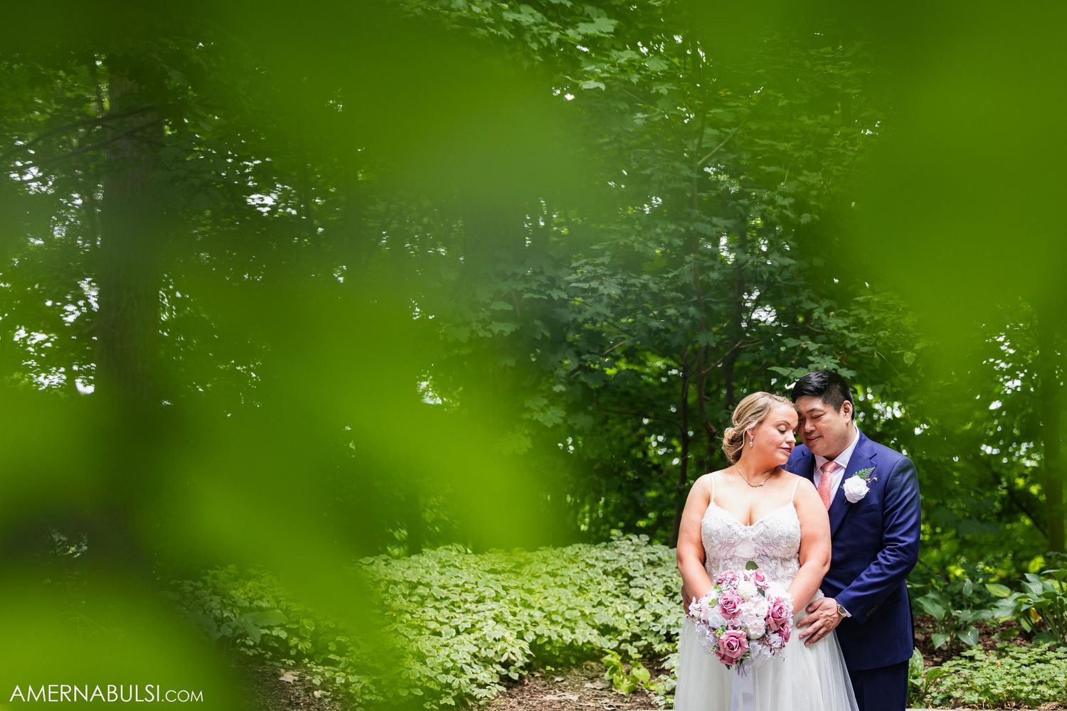 Artistic wedding portrait framed by lush green foliage in a garden setting.