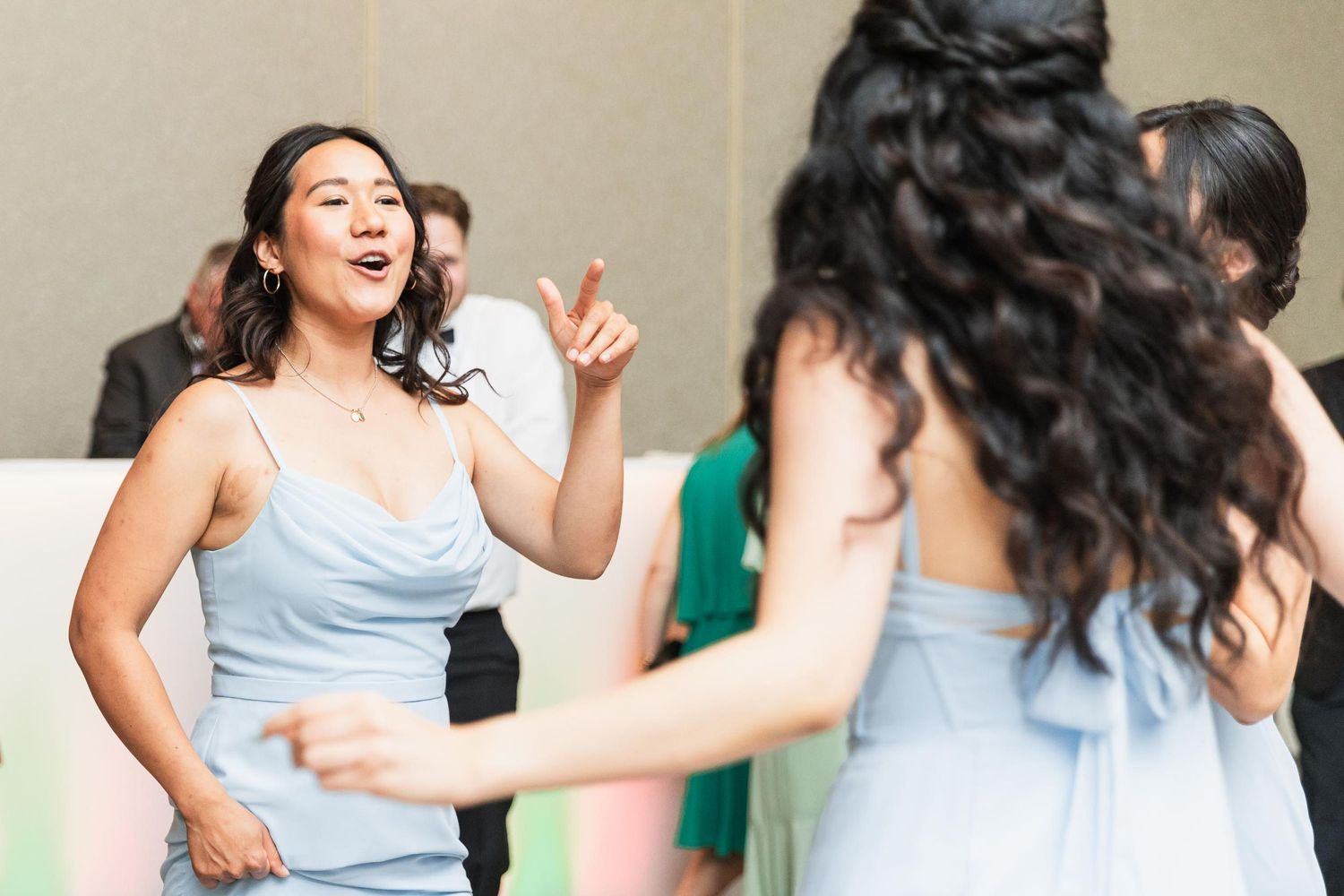 Bridesmaids in light blue dresses dance joyfully at a wedding reception.