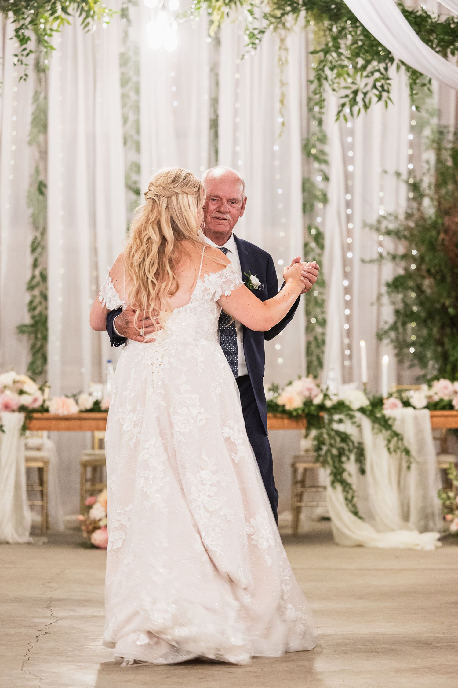 Couple dancing together in beautifully decorated wedding venue with white drapes and floral arrangements.