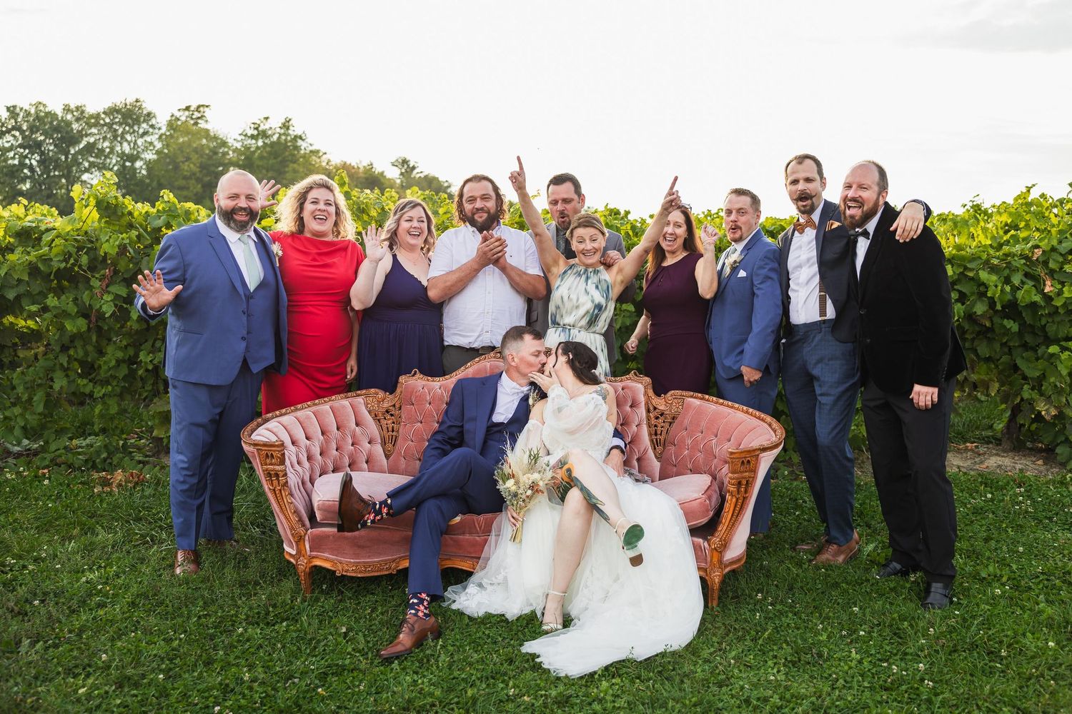 Wedding party poses together on vintage pink couch in vineyard setting.