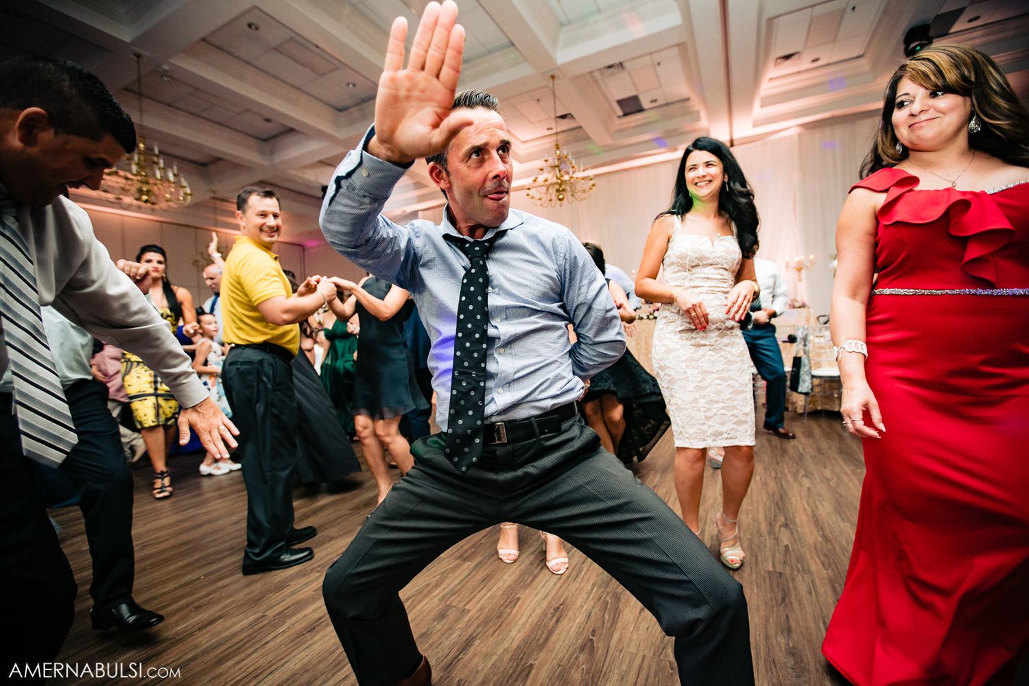 Wedding guests dance energetically on a wooden floor at a reception celebration.