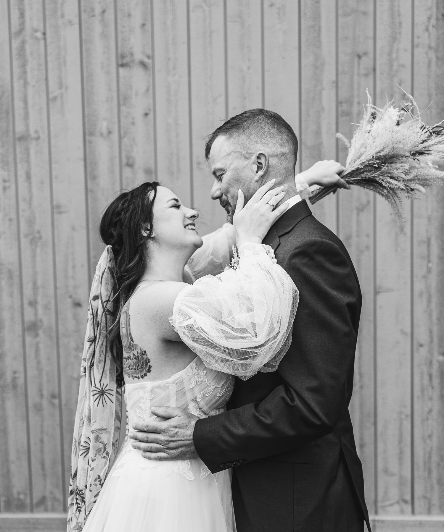 Romantic black and white portrait of newlyweds sharing intimate moment against rustic wall.
