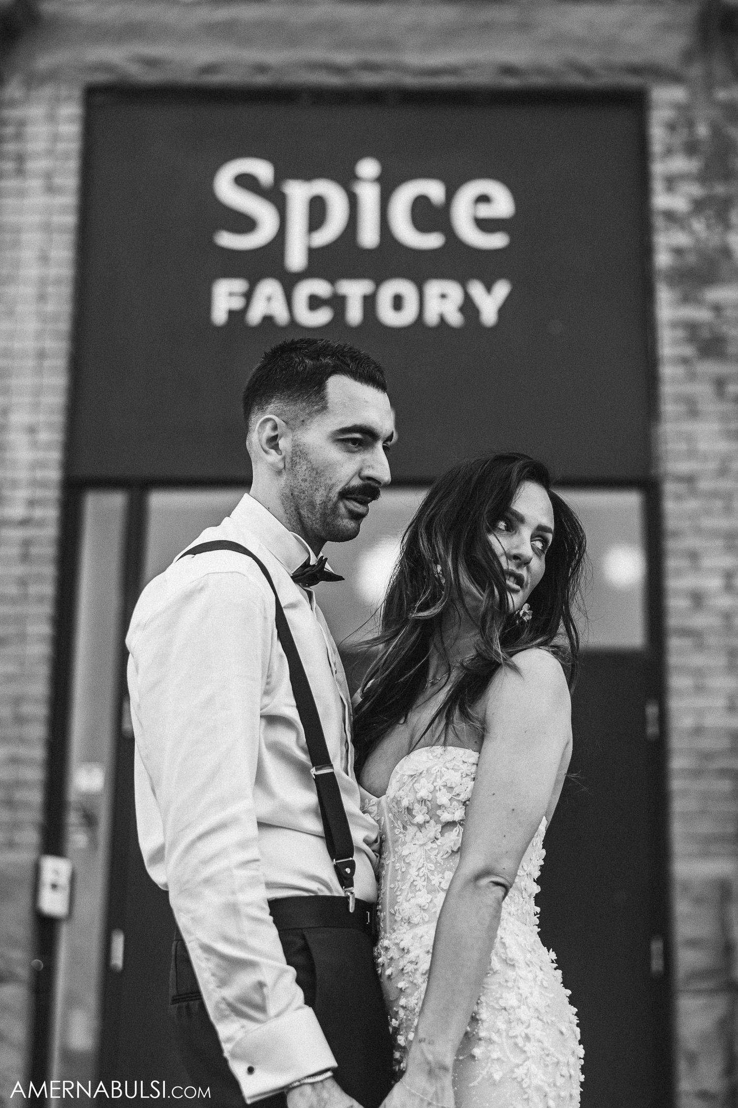 Black and white portrait of couple in formal attire in front of Spice Factory sign.