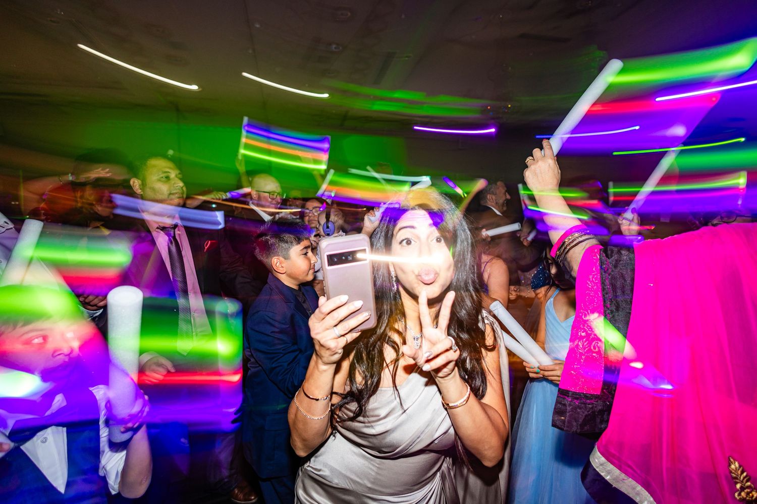Crowd enjoying a lively dance party under neon green and purple lights in a nightclub setting.