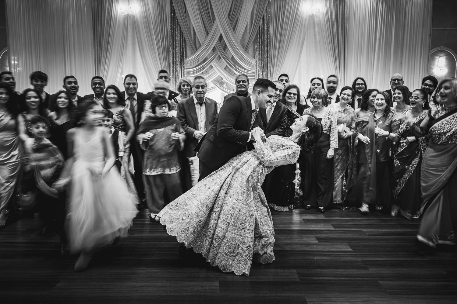 Black and white photo of wedding guests watching a couple dancing at an elegant reception venue.