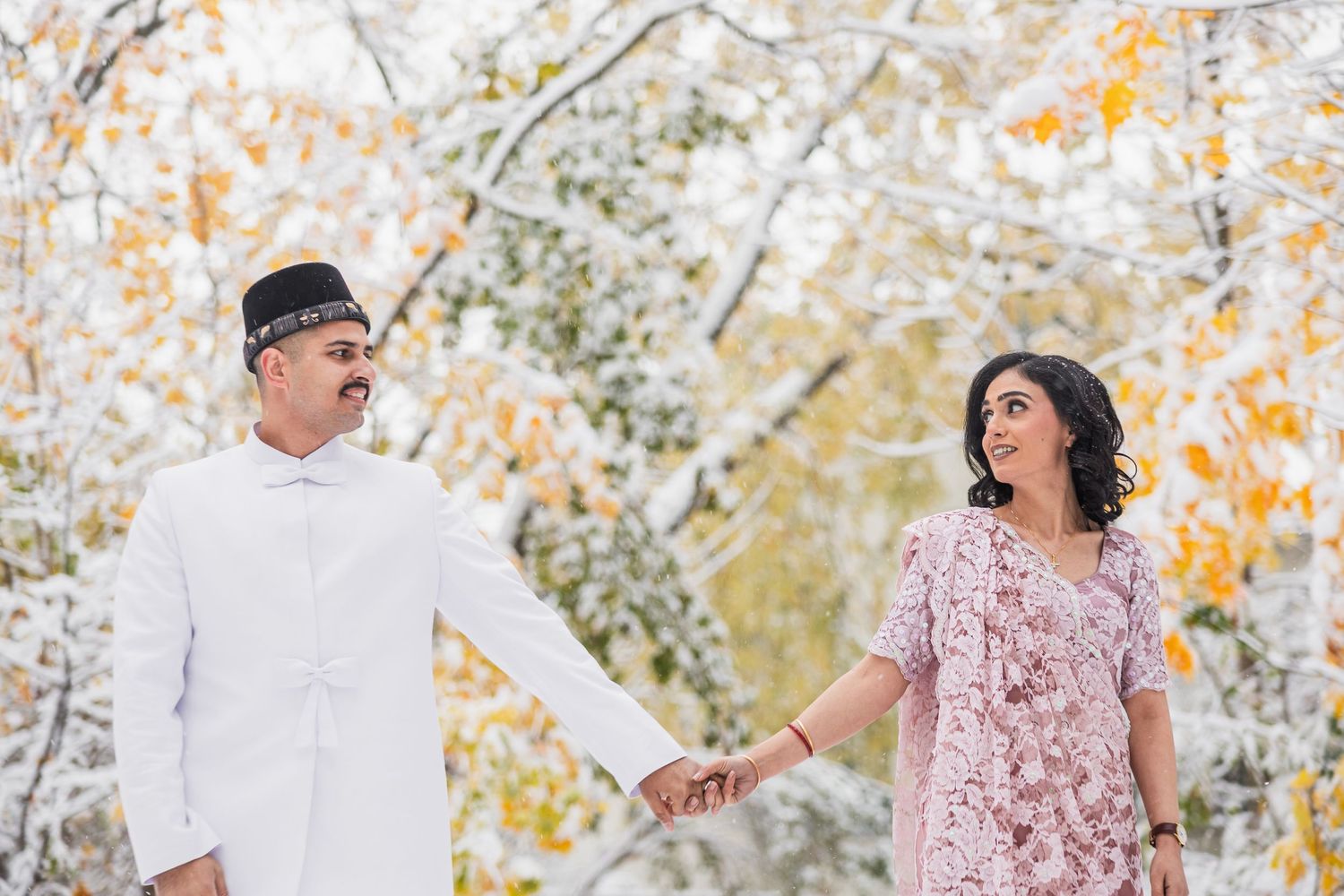 Couple shares a joyful moment together in autumn forest with snow-covered branches.