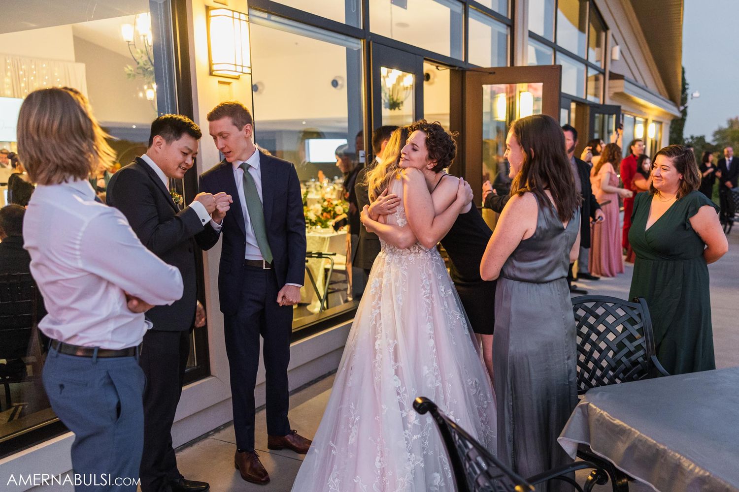 Wedding guests mingle during cocktail hour outside a venue with large glass windows.