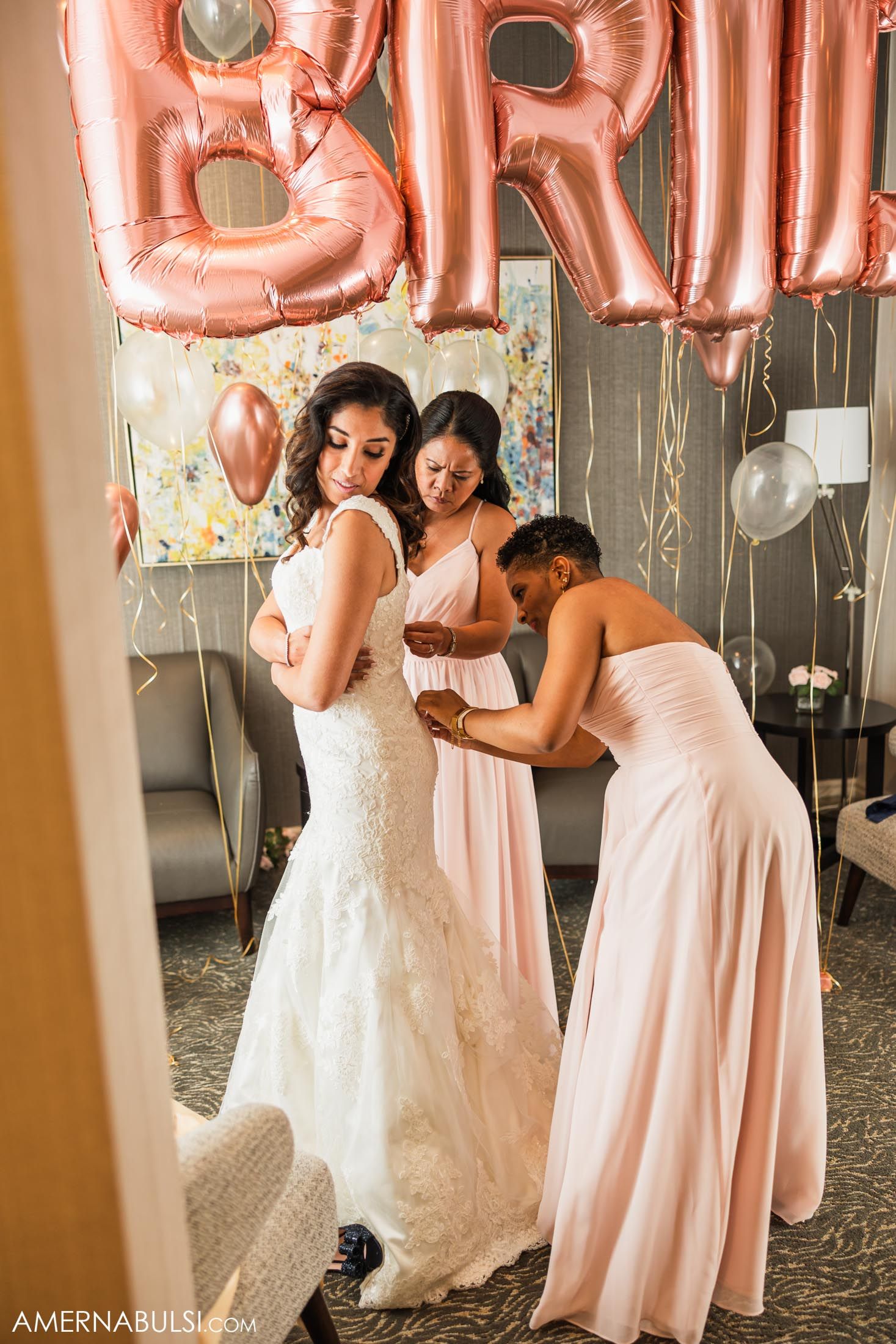 Final dress adjustments being made during bridal preparation under rose gold balloon letters.