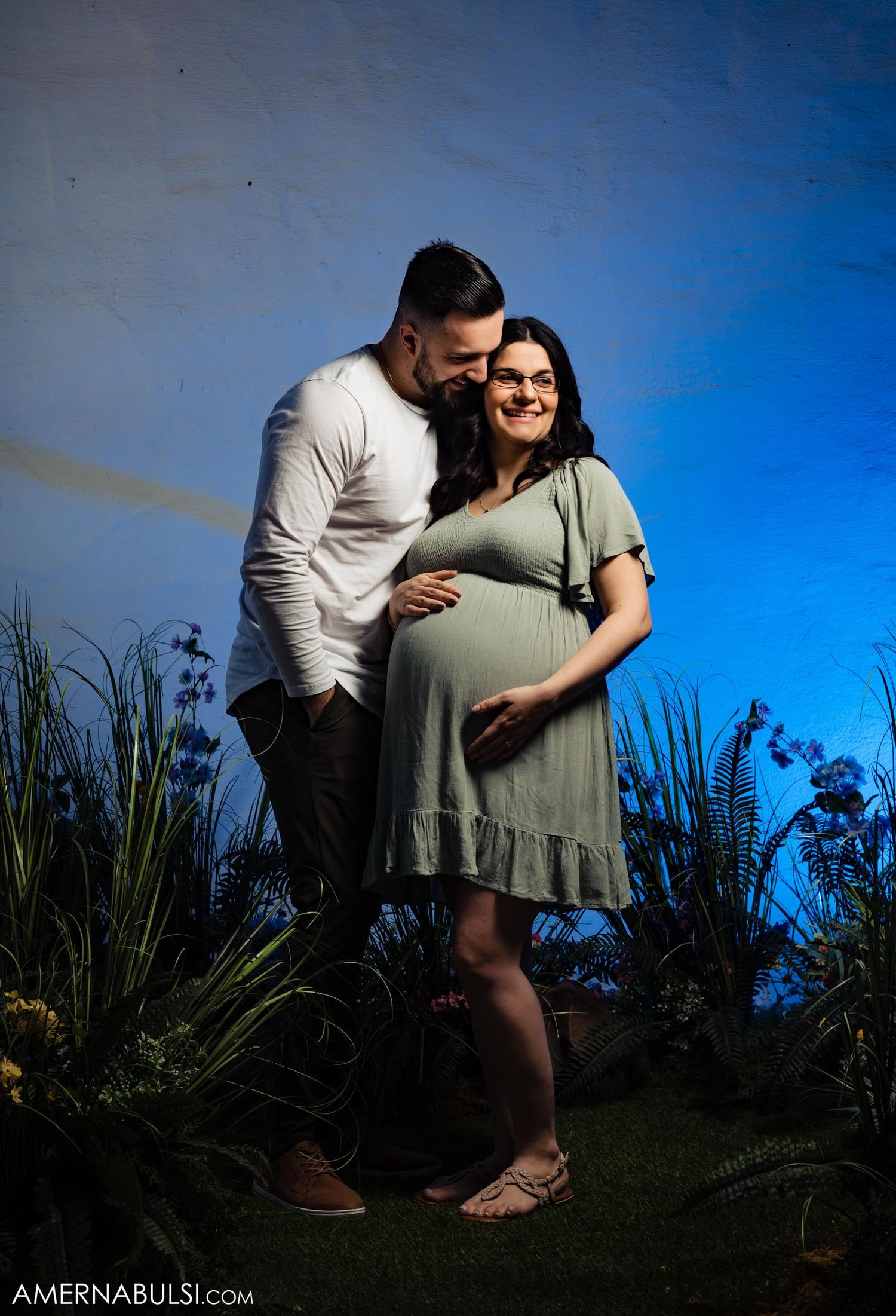 An intimate maternity portrait with dramatic lighting and natural backdrop.