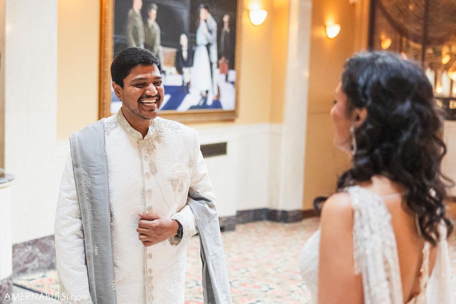 A joyful moment during a first look wedding reveal in an elegant hallway setting.