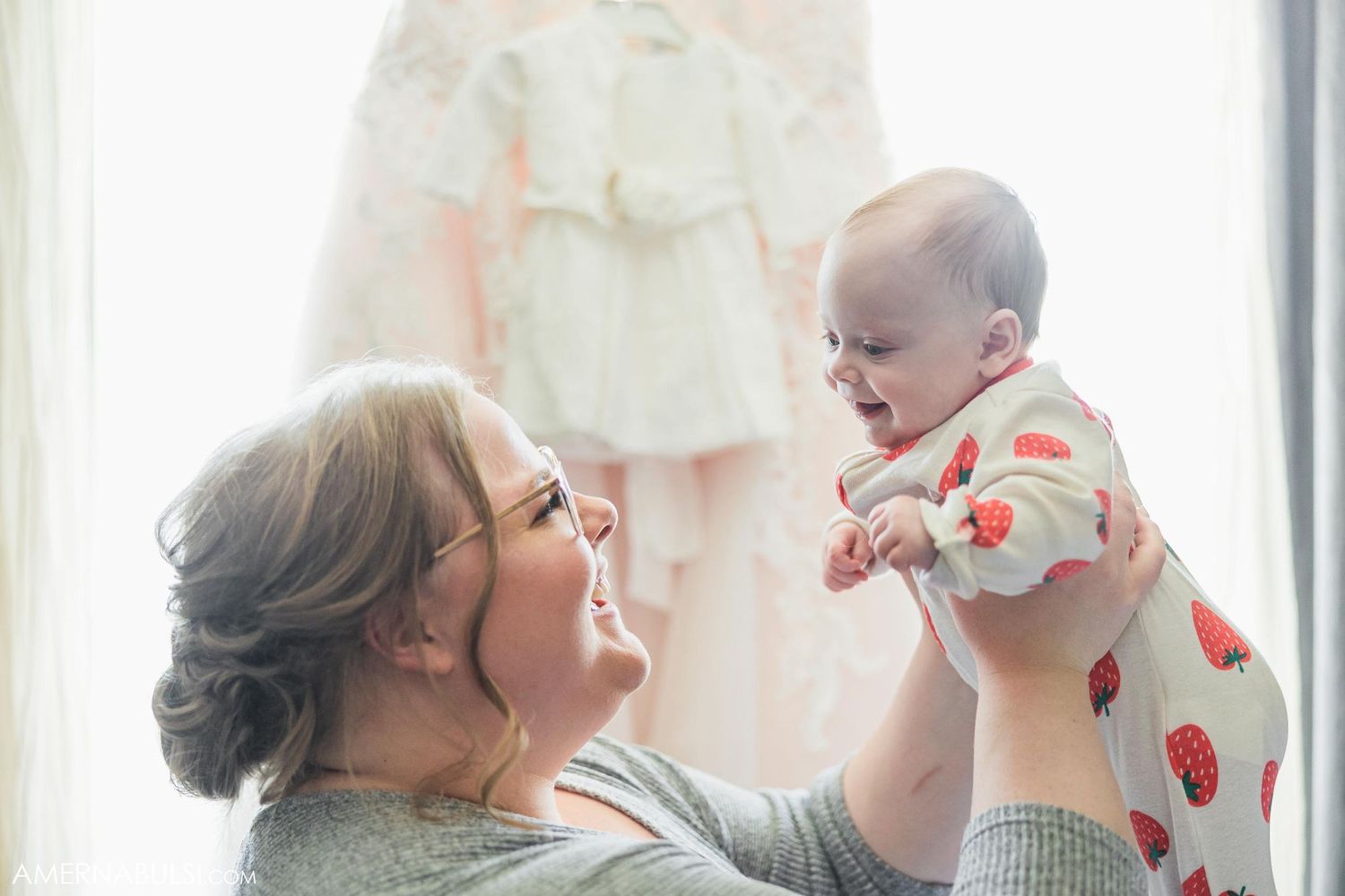 Joyful moment shared between parent and laughing baby by wedding dress display.