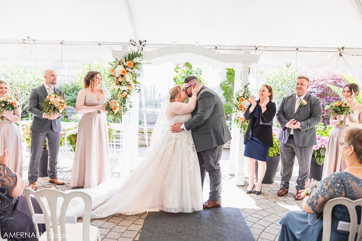 Couple sharing their first kiss during outdoor tent wedding ceremony surrounded by guests.
