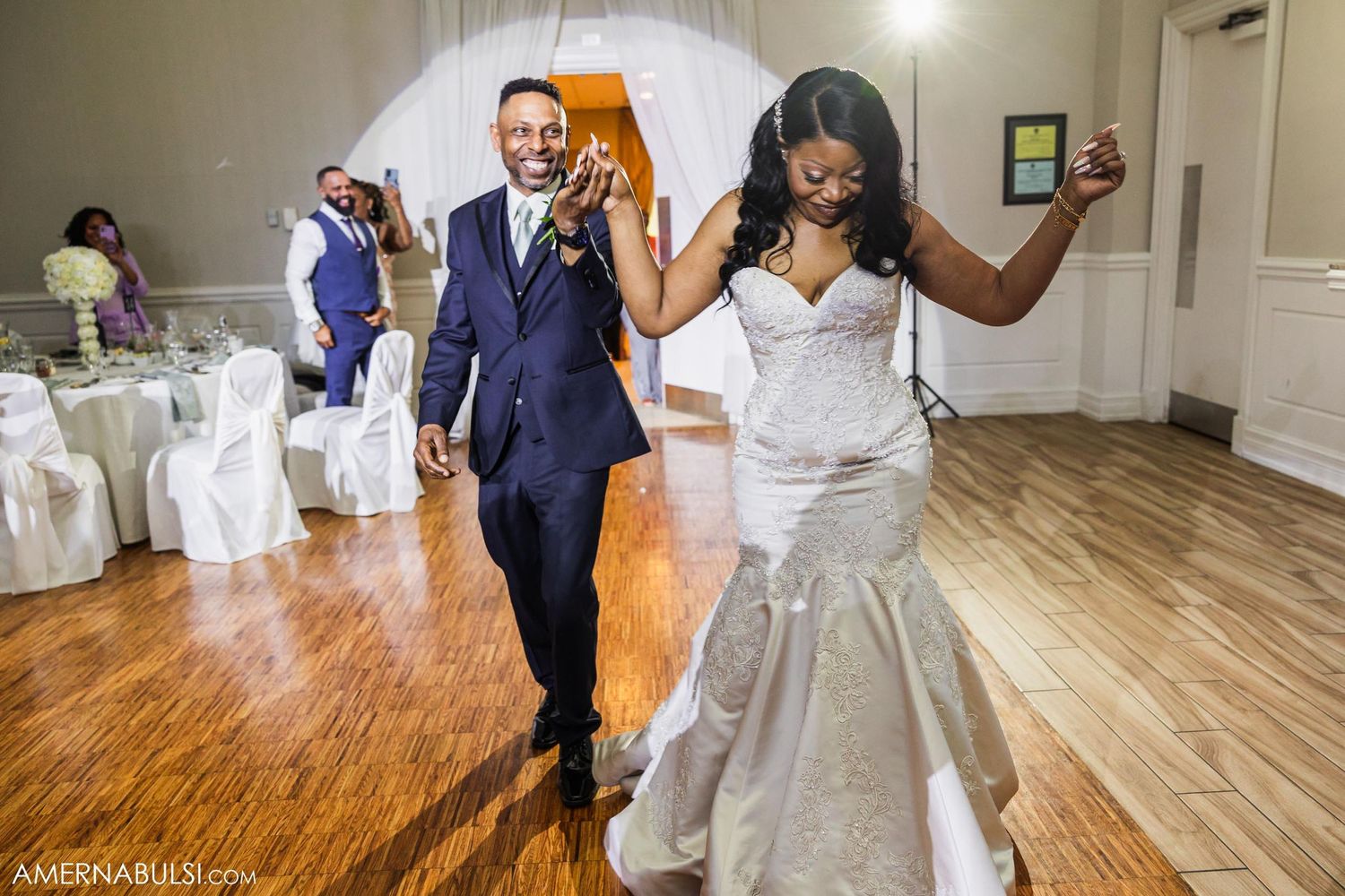 Couple dancing and celebrating during wedding reception on hardwood floor with decorative backdrop.