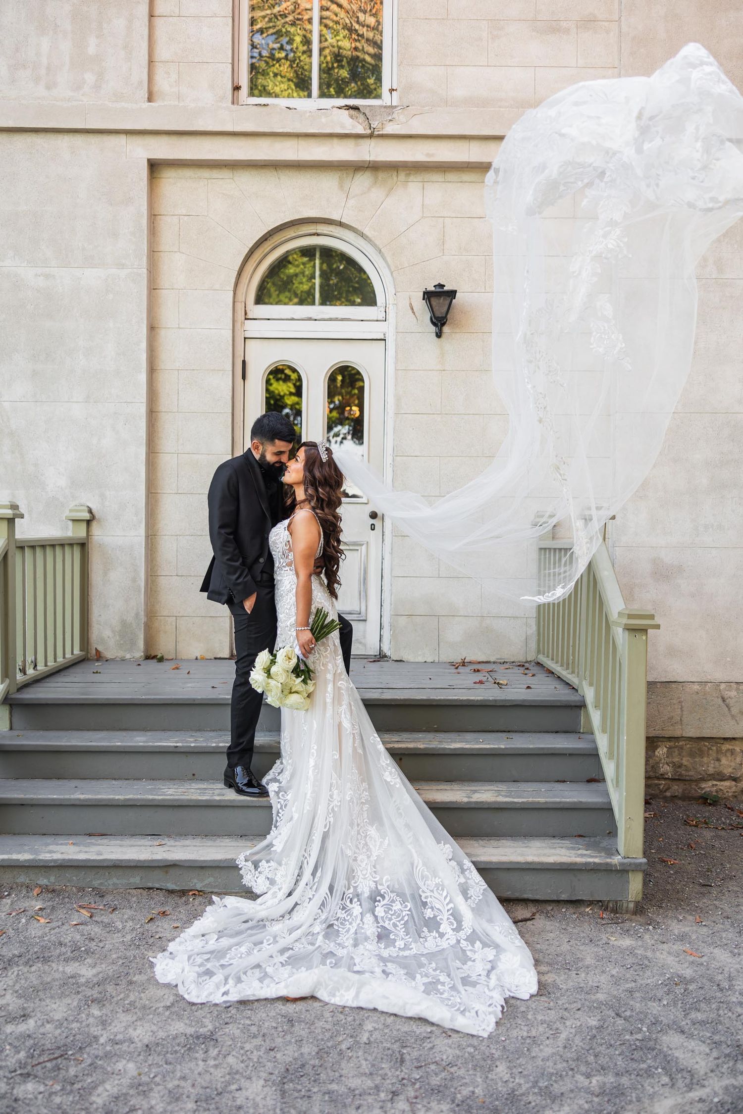 Bride's veil flows dramatically during intimate moment on mansion steps.