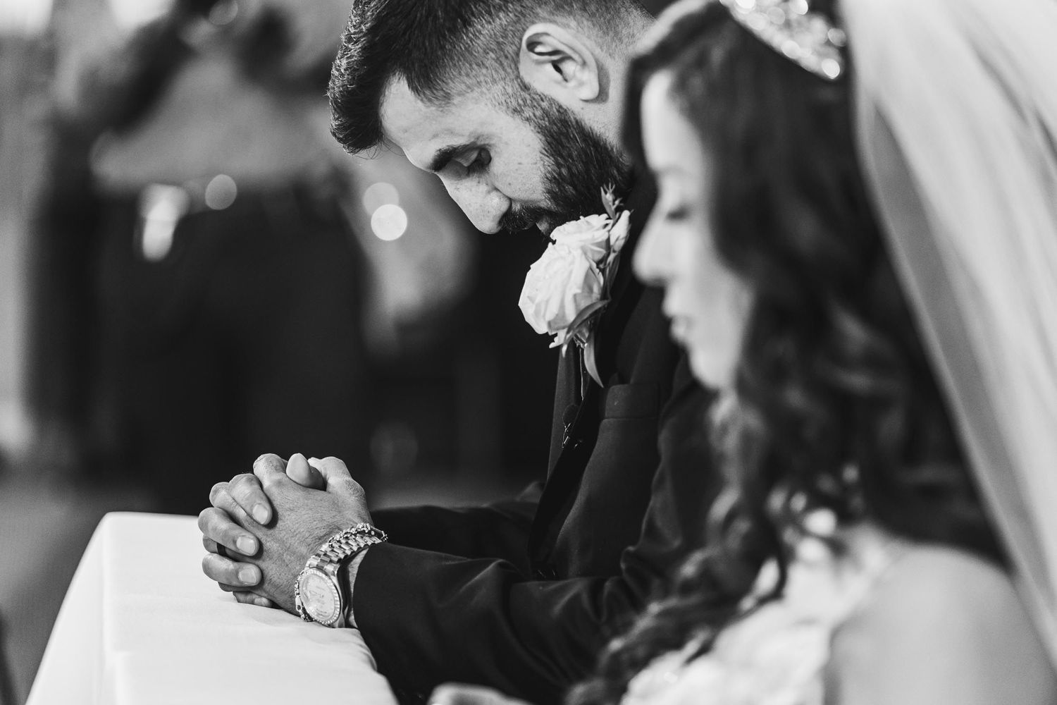 A black and white photo captures an intimate moment of prayer during a wedding ceremony.