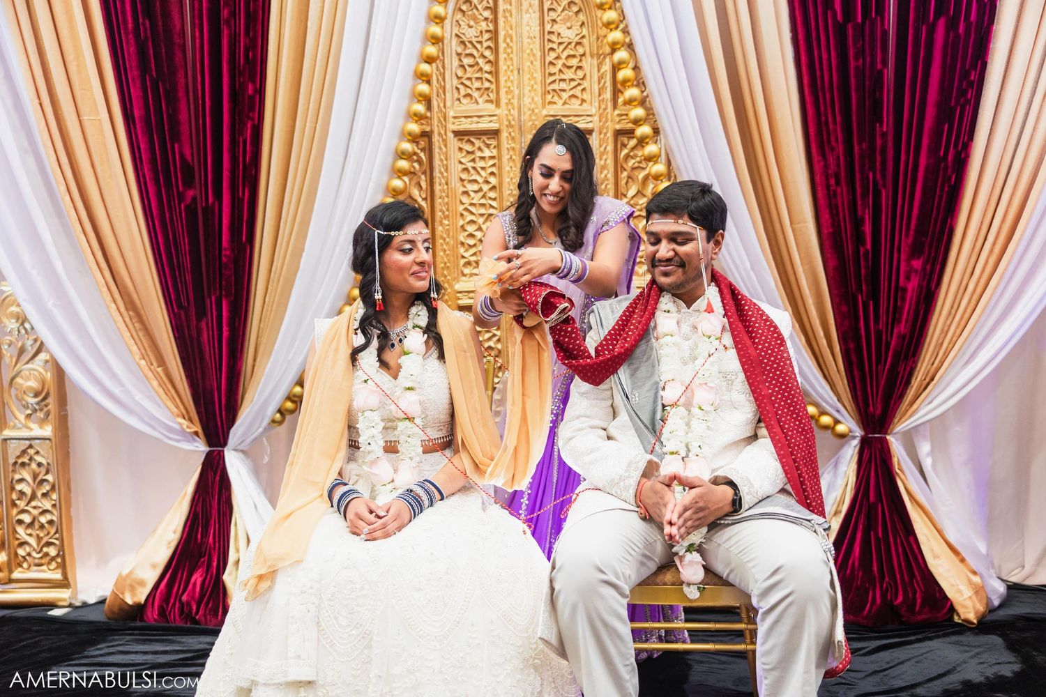 Couple shares joyful moment during traditional Indian wedding ceremony with ornate gold backdrop.