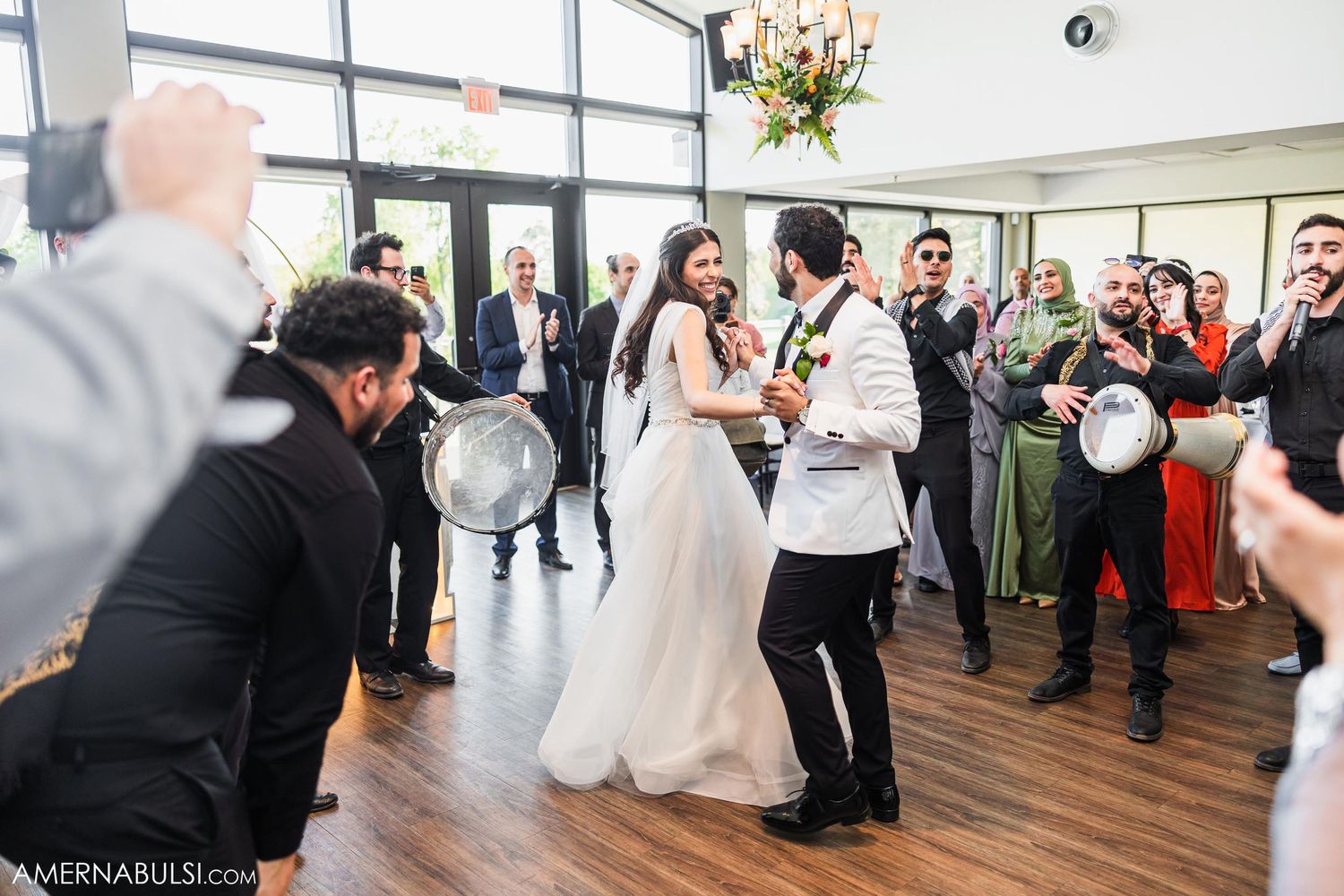 Newlyweds celebrate on dance floor while guests cheer with tambourines and percussion.