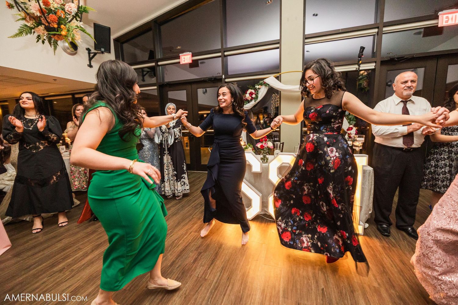 Party guests in formal attire dancing together on a wooden floor during a festive celebration.
