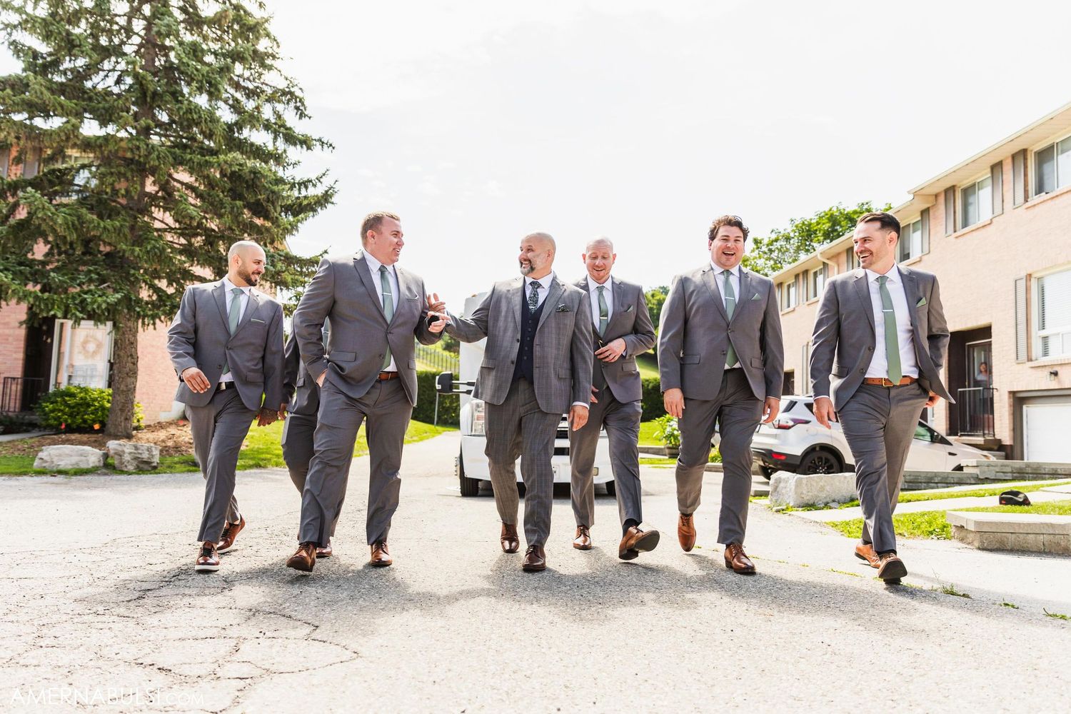 Groomsmen in grey suits walking together outdoors in synchronized motion.