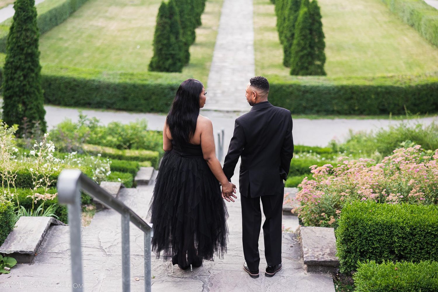 Couple in formal wear descending garden steps lined with cypress trees.