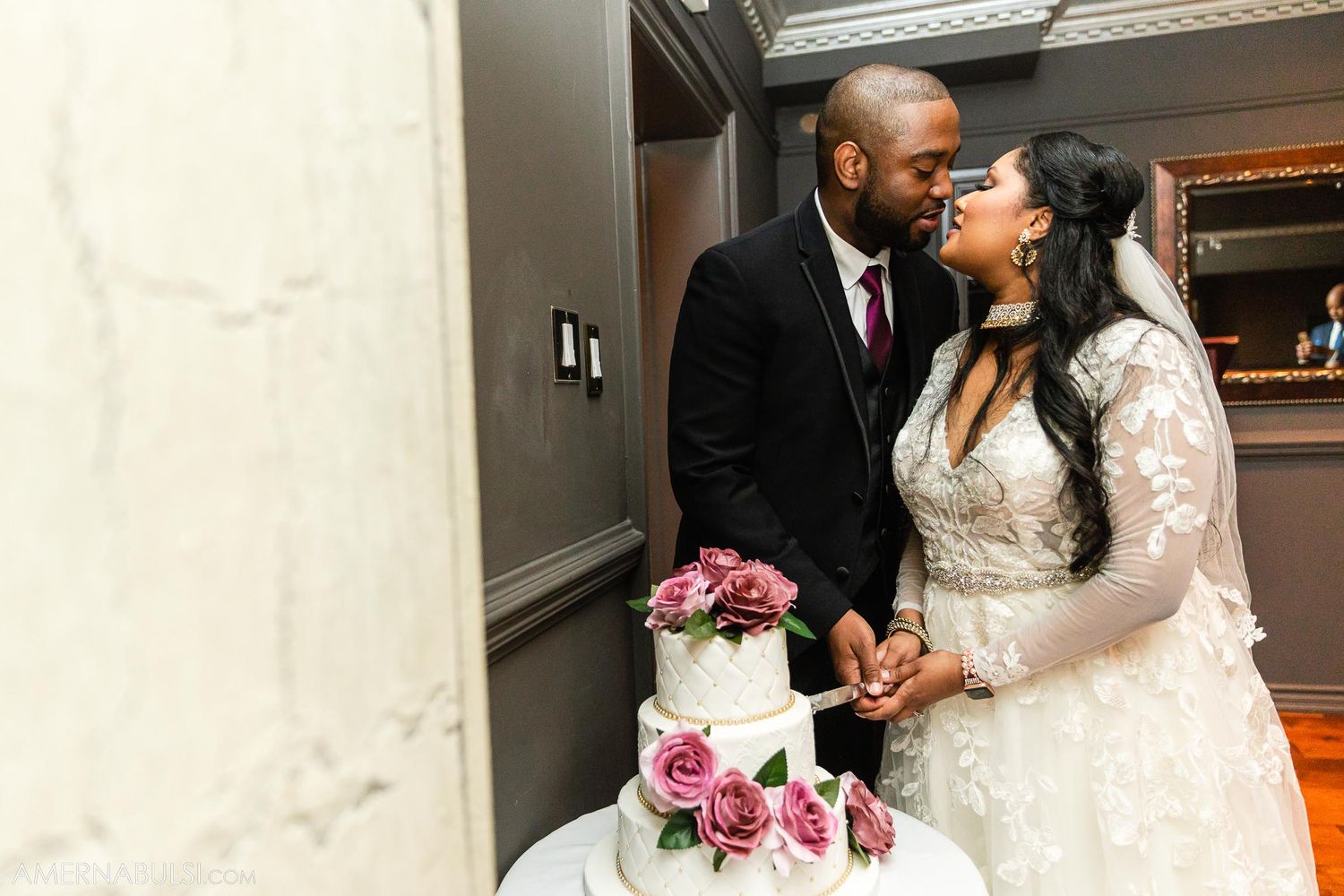 Newlyweds share an intimate moment next to their elegant wedding cake decorated with pink and white flowers.