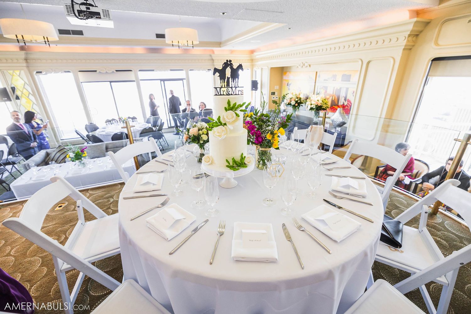 An elegant wedding reception table setting with floral centerpiece and white linens.