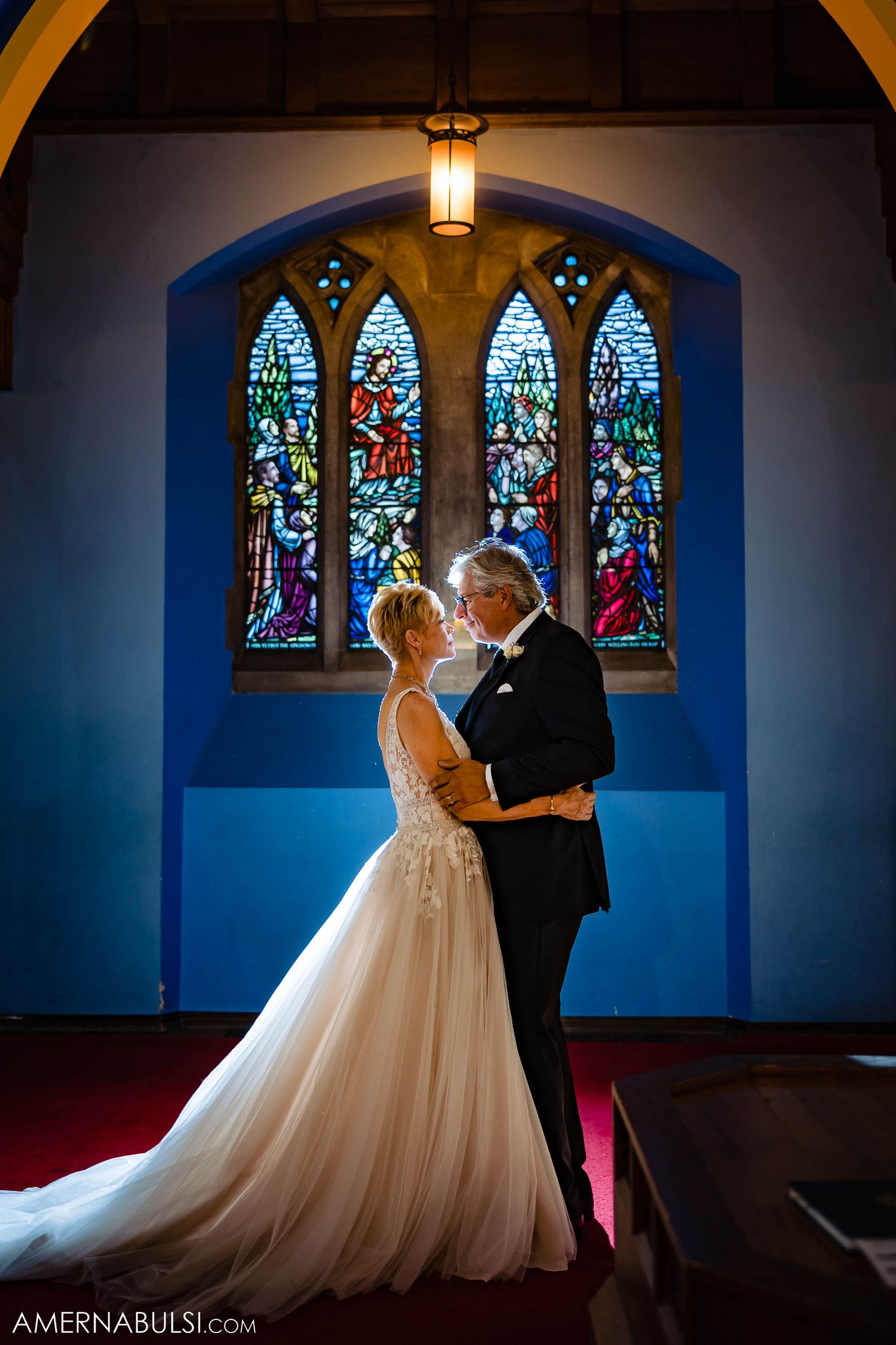 A romantic wedding portrait captured in front of illuminated stained glass church windows.