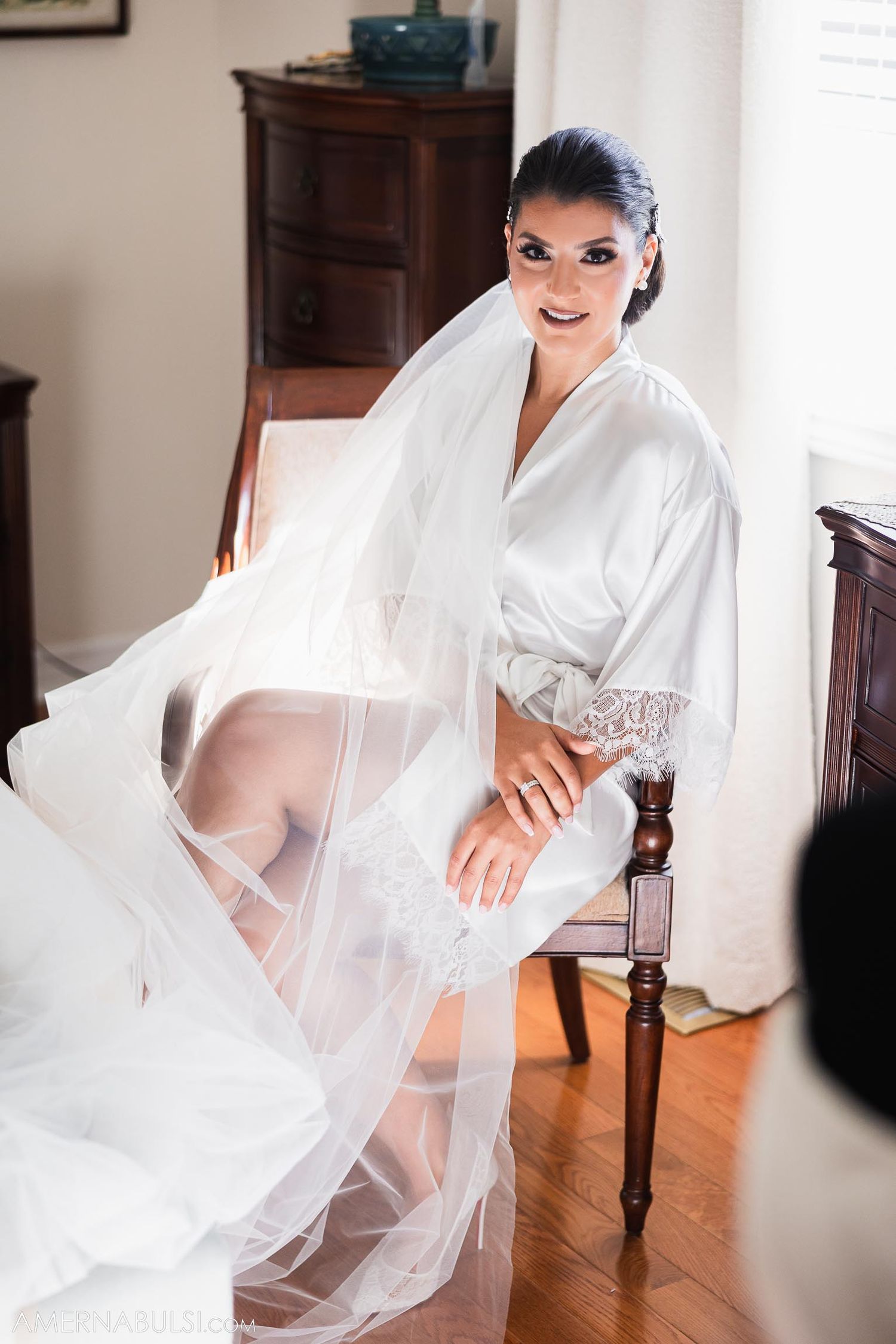 Preparation photo showing flowing white bridal robe in sunlit room.