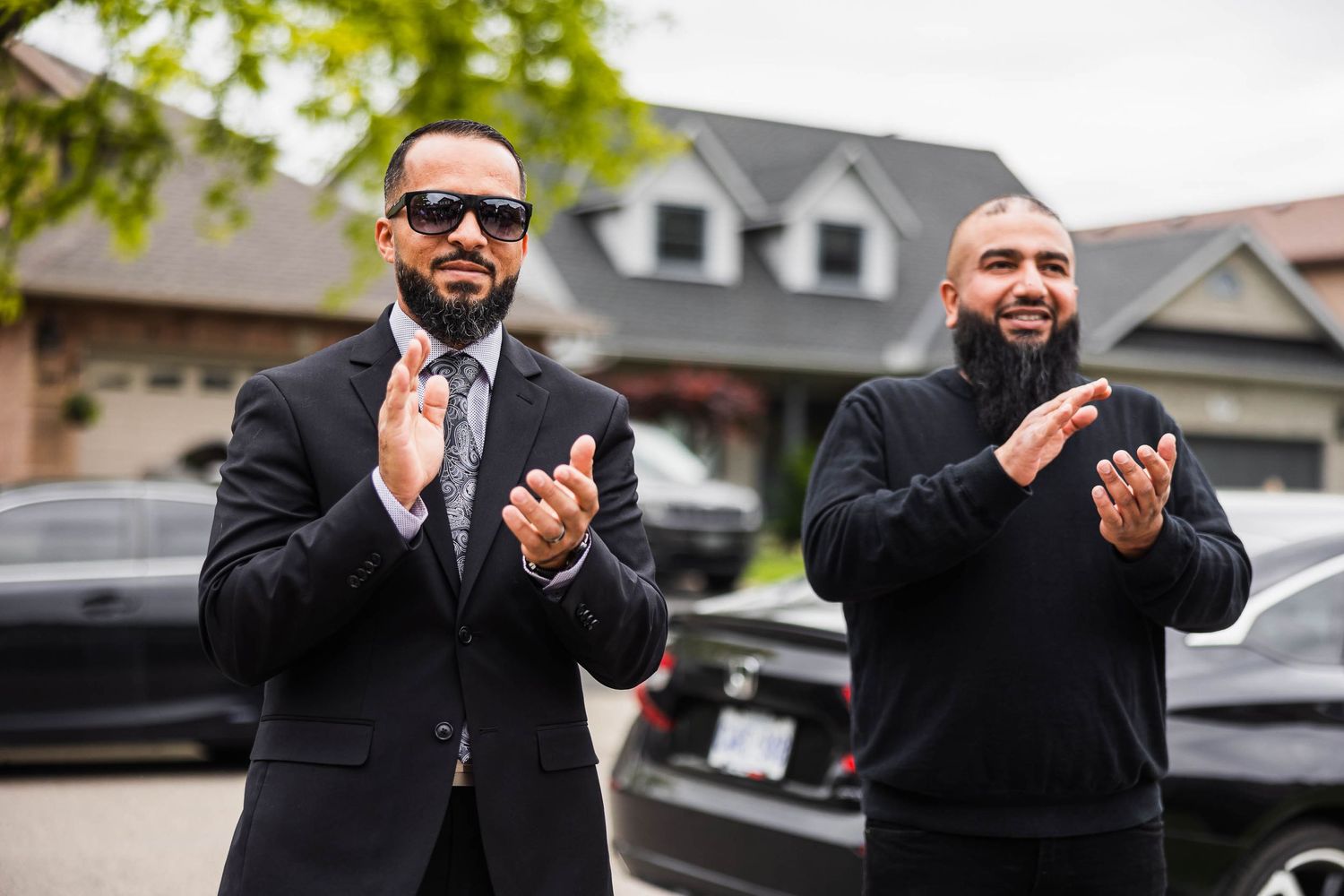 Two wedding guests in suits clapping outdoors.