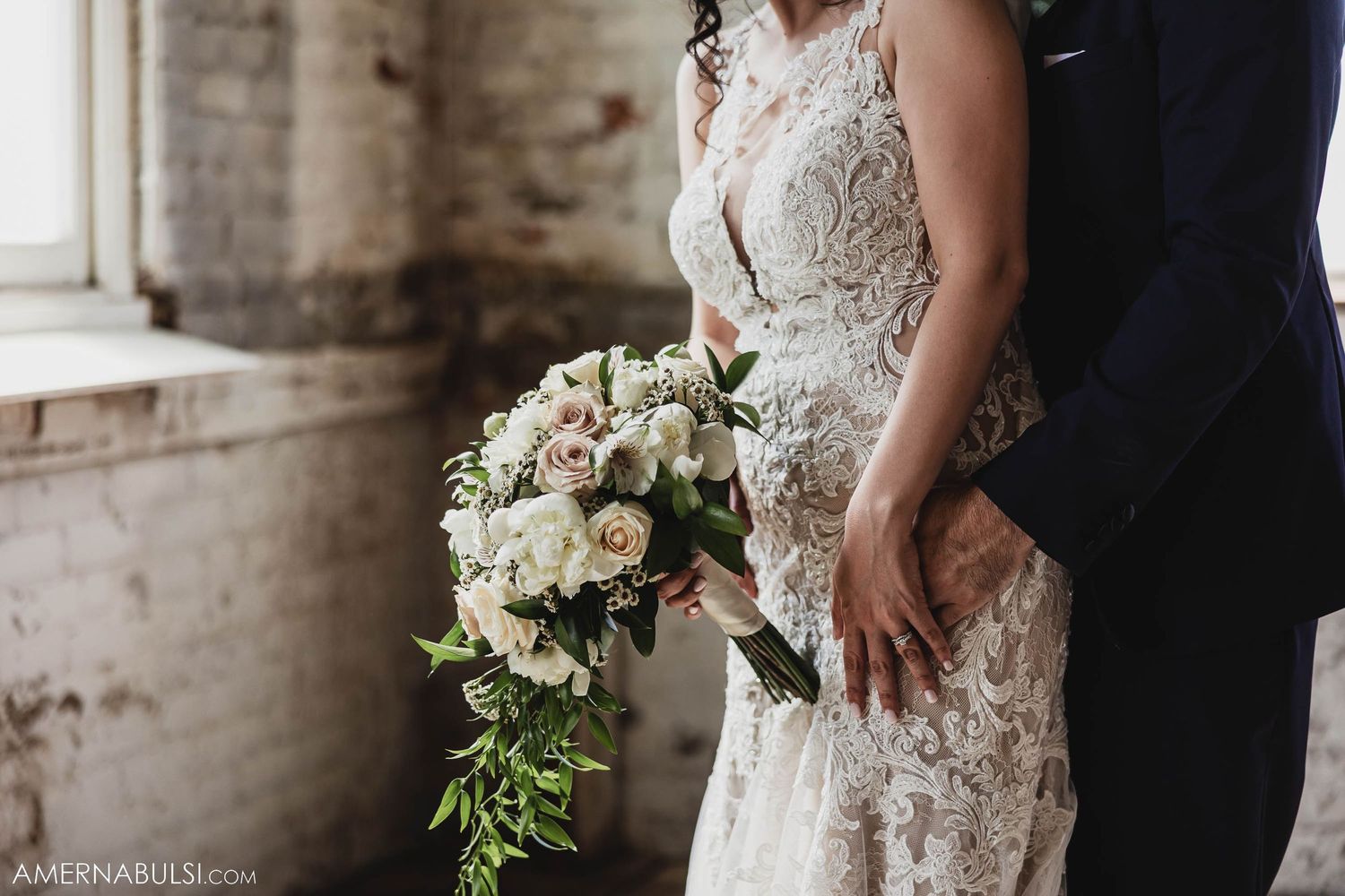 Close-up of cascading white and green bridal bouquet against lace wedding dress.
