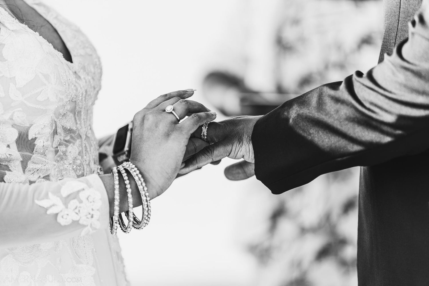 Black and white close-up of hands exchanging rings during wedding ceremony.