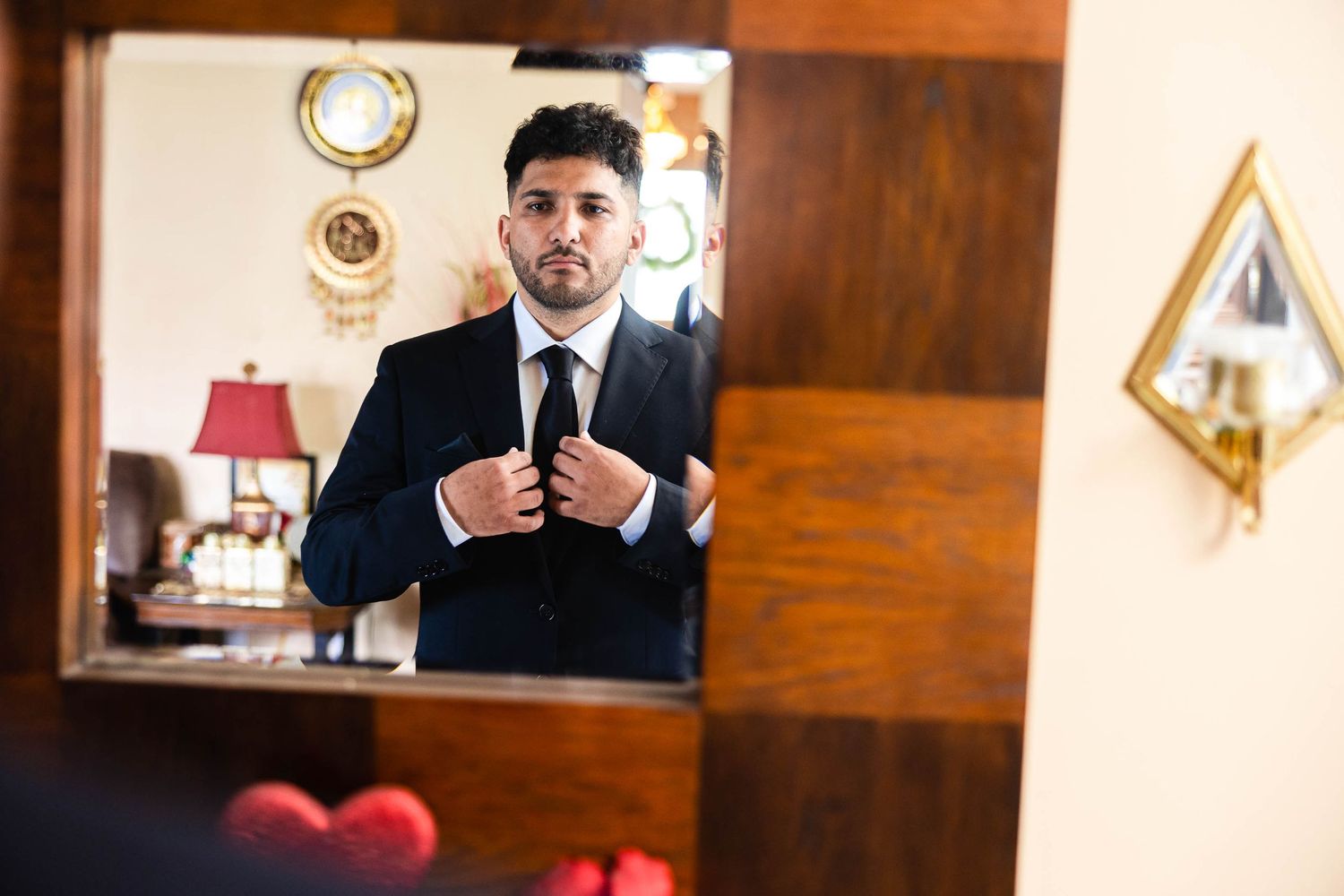 A reflection of a man adjusting his tie in an elegant wooden-framed mirror.